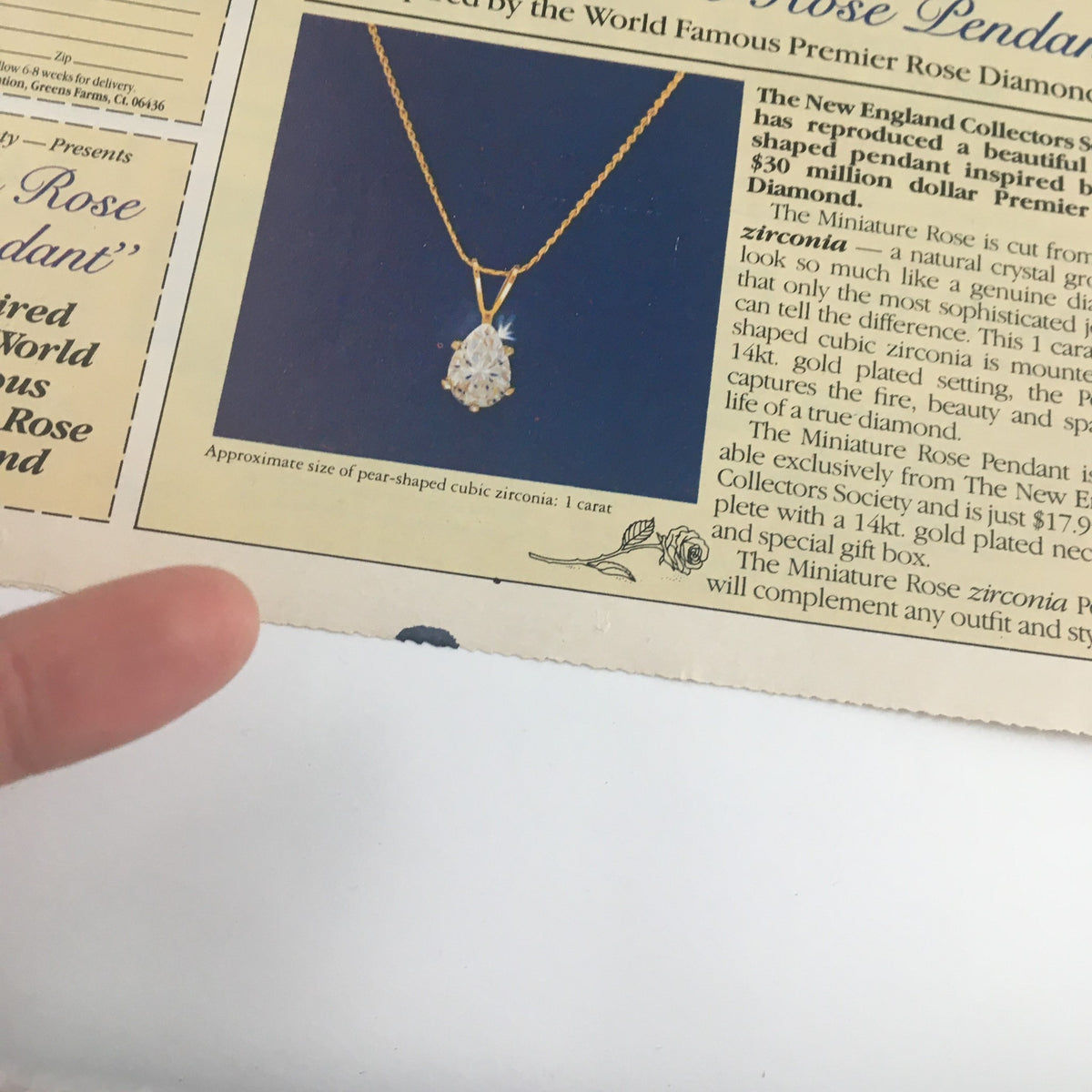 Close-up image of a pendant inspired by the World Famous Premier Rose Diamond from the New England Collectors Society, displayed with a finger for scale. Showcasing the intricate design of the cubic zirconia pendant.