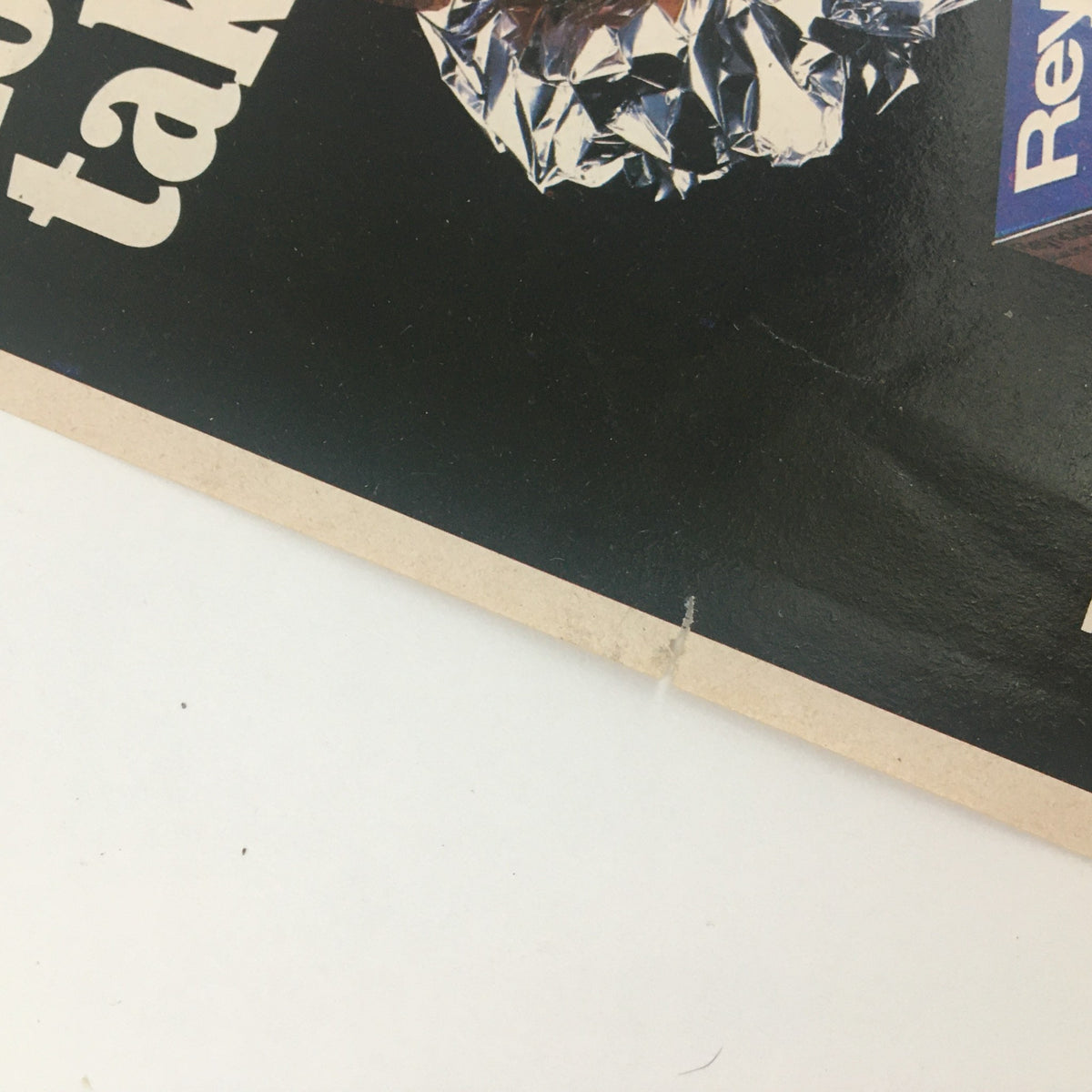 Close-up view of a 1983 Reynolds Wrap Aluminum Foil Circular Coupon Advertisement showing slight wear and a small rip, emphasizing its vintage condition.