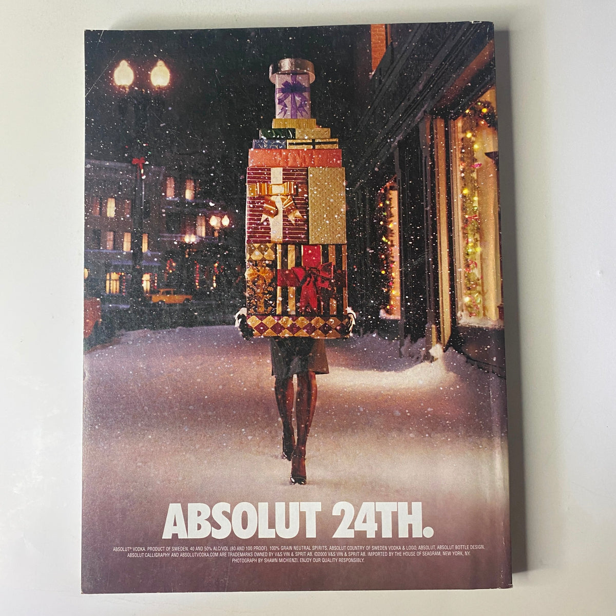 Holiday-themed advertisement showing a woman carrying a large stack of wrapped gifts, set in a snowy urban environment with text reading 'ABSOLUT 24TH,' from Vogue Magazine December 2000 Nicole Kidman Cover.