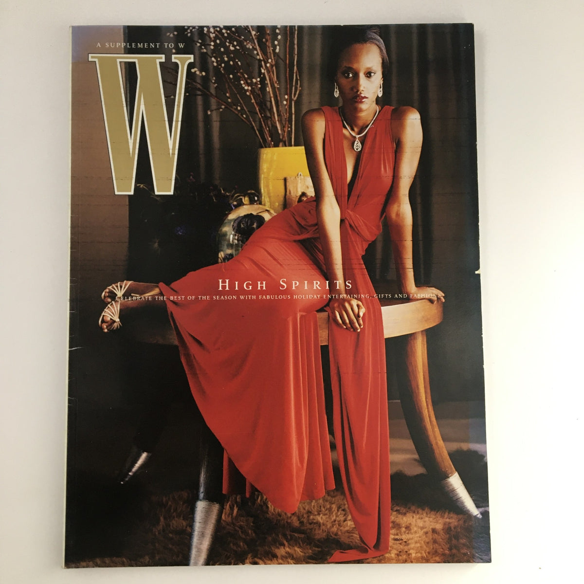 W Magazine 2005 Holiday Fashion & Gift Book High Spirits, showcasing a model in a stylish red gown seated elegantly, embodying early 2000s fashion trends and holiday spirit.