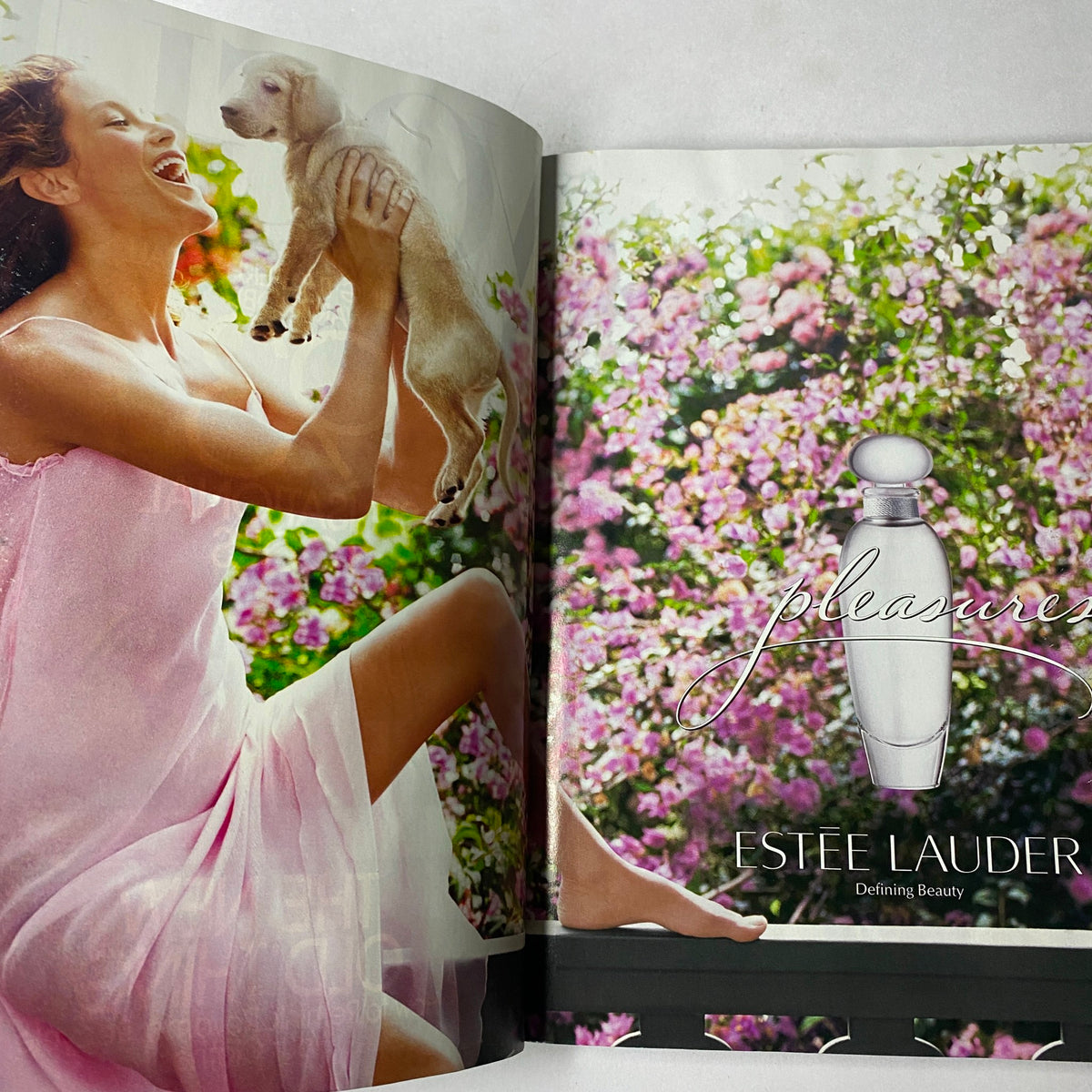 Double page spread from October 2002 Vogue Magazine featuring an Estee Lauder fragrance advertisement with a woman joyfully playing with a puppy amidst beautiful flowers.
