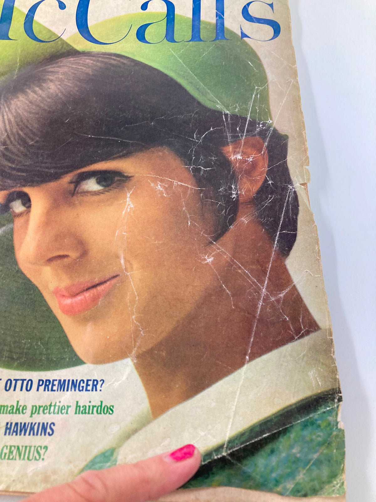 Close-up view of the Vintage McCall's Magazine March 1965 cover, highlighting the woman's face and stylish green hat, with noticeable wear and creases.