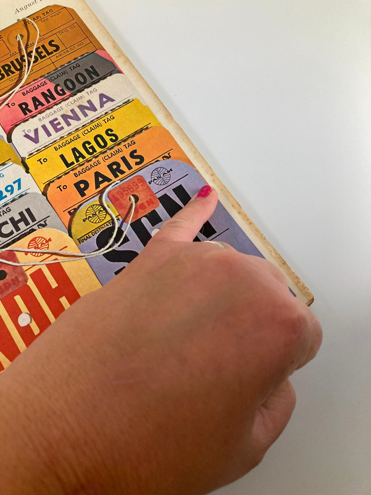 Close-up of vintage luggage tags from the VTG Fortune Magazine August 1962, showcasing travel destinations including Brussels, Rangoon, and Paris.