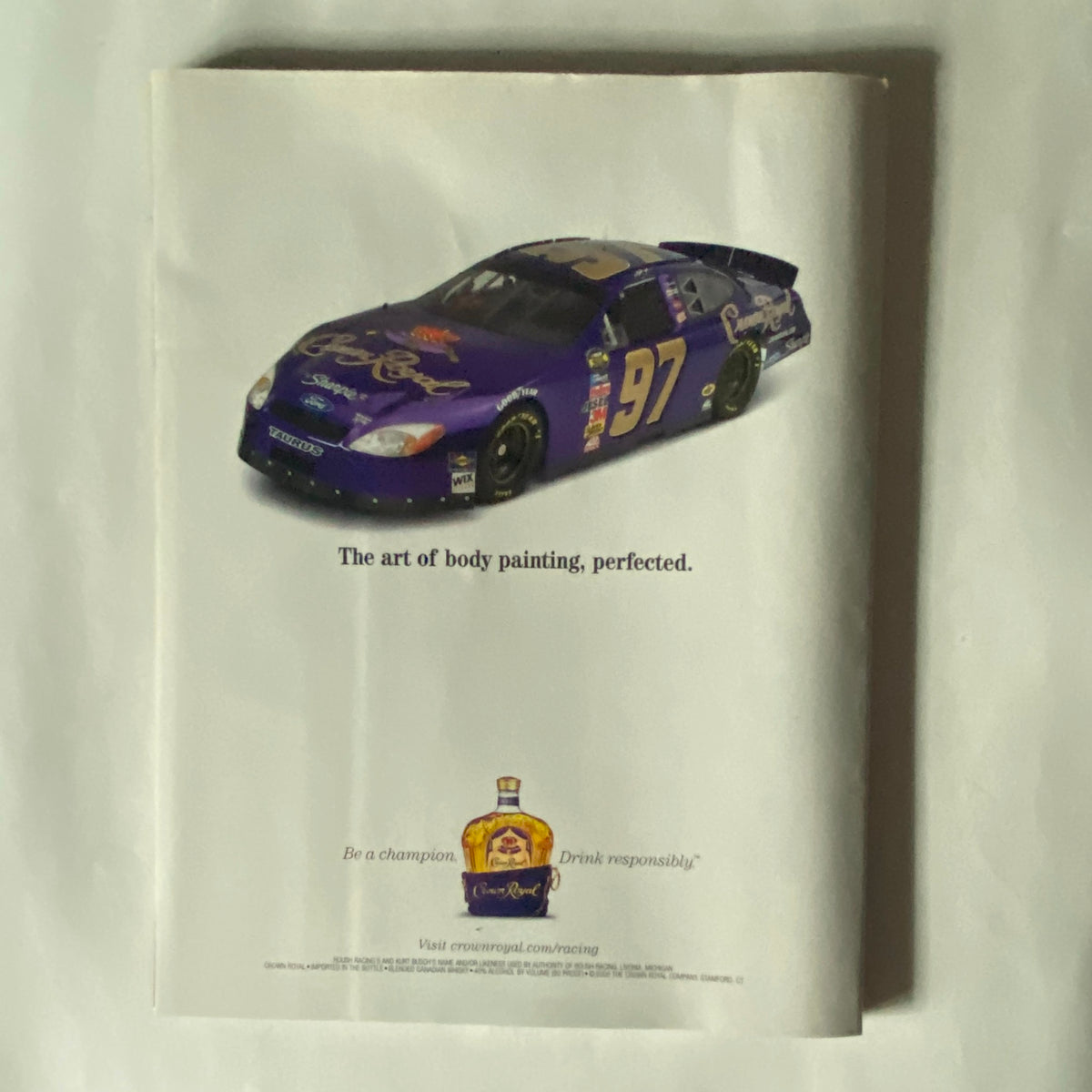 Advertisement page in Sports Illustrated Winter 2005 Carolyn Murphy Swimsuit Issue featuring a purple NASCAR car, promoting the art of body painting and related events.