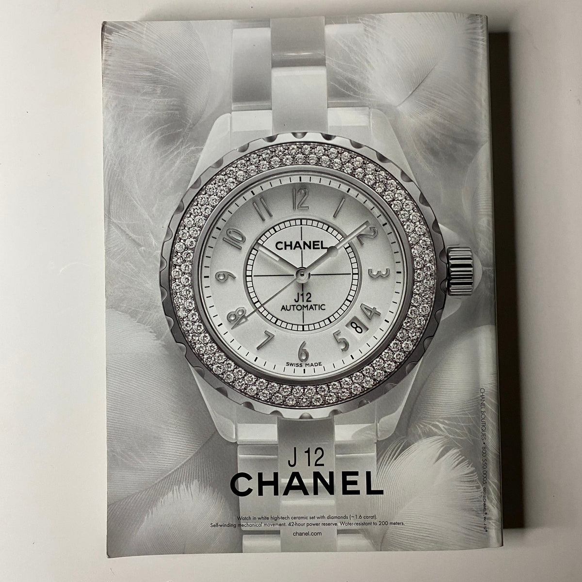 Back cover of Vogue Magazine March 2012 showcasing a luxurious Chanel J12 watch with a diamond bezel against a soft feather background.
