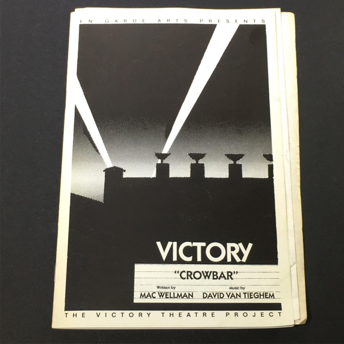Cover image for 'Victory Crowbar' by Richard Caliban, presented by En Garde Arts, featuring dramatic lighting from a rooftop.