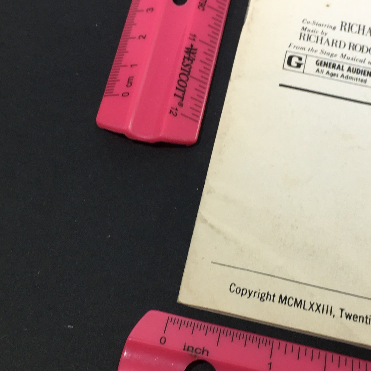 Close-up view of the back cover of the vintage pressbook for 'The Sound of Music,' indicating copyright information and dimensions, surrounded by pink rulers for scale.