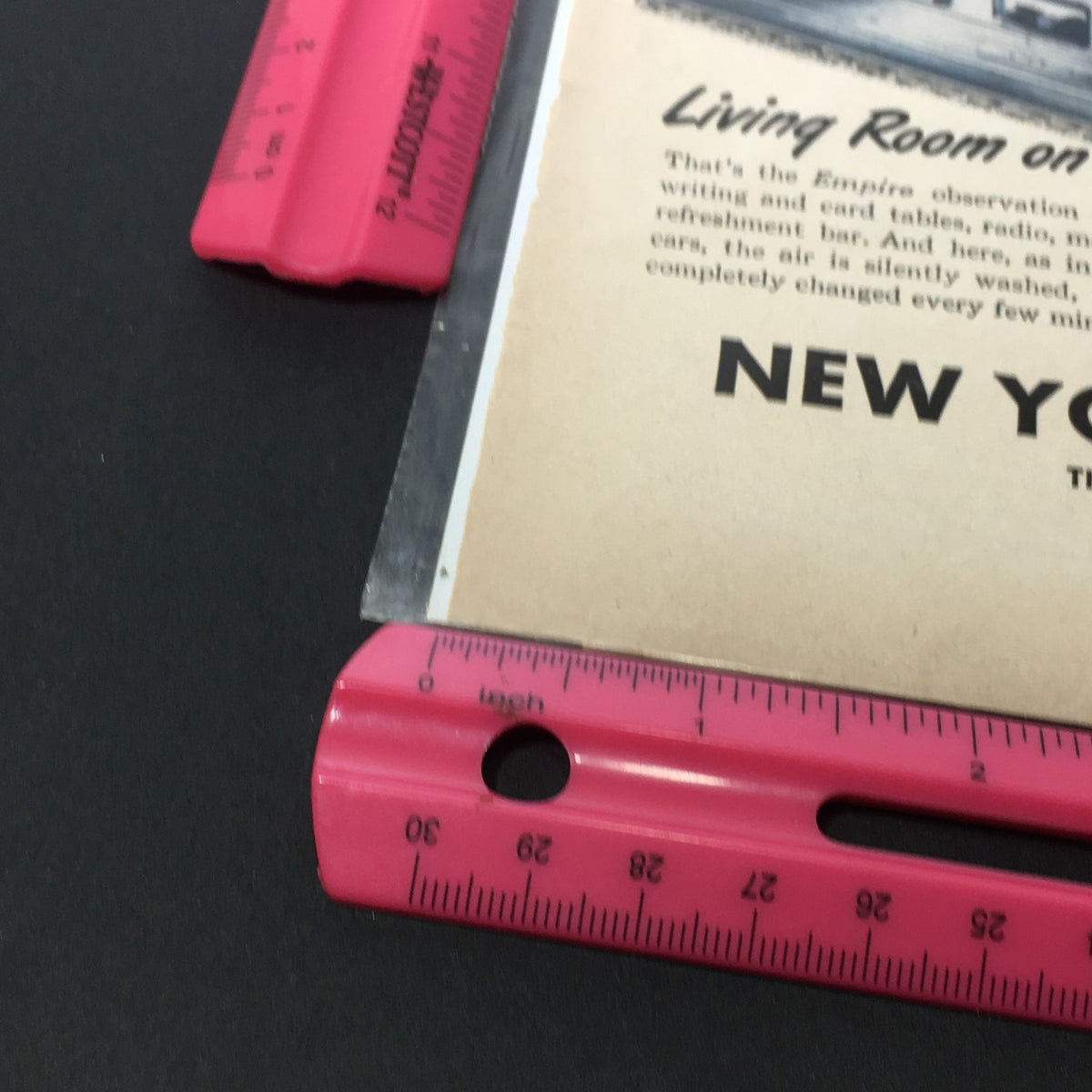 Close-up of the lower section of the 'VTG 1941-1945 New York Central System Empire Trains Print Ad' with a ruler indicating size, highlighting the advertisement's text and vintage details.