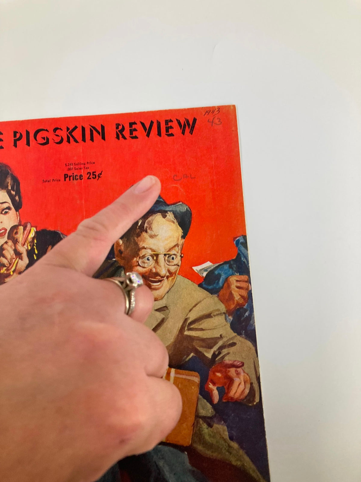 Close-up of the cover of the 1943 NCAA Football USC Trojans vs USC Golden Bears Pigskin Review, showing a hand pointing at handwritten notes and minor wear on the cover, emphasizing the program's age and authenticity.