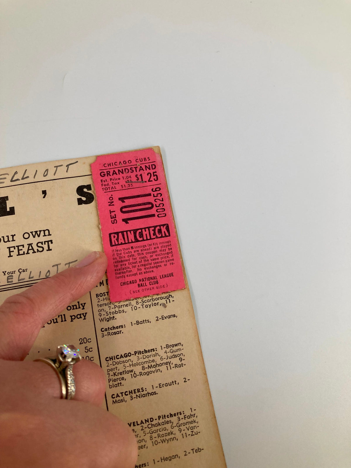 A hand holding a grandstand rain check ticket from the 1951 MLB Chicago Cubs vs Boston Red Sox game, with restaurant menu details in the background.