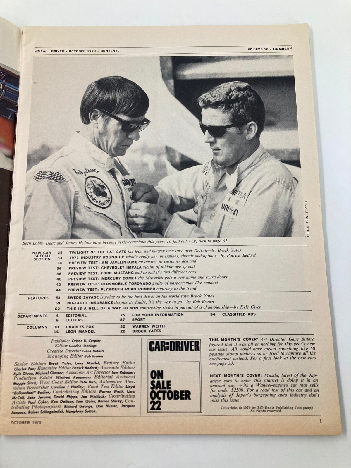 Car and Driver Magazine October 1970 featuring Bobby Isaac and James Hylton in a candid moment. The image depicts both drivers preparing for a race with a focus on their racing suits and sunglasses, showcasing the vintage automotive culture of the era. Perfect for collectors and enthusiasts of motorsport history.