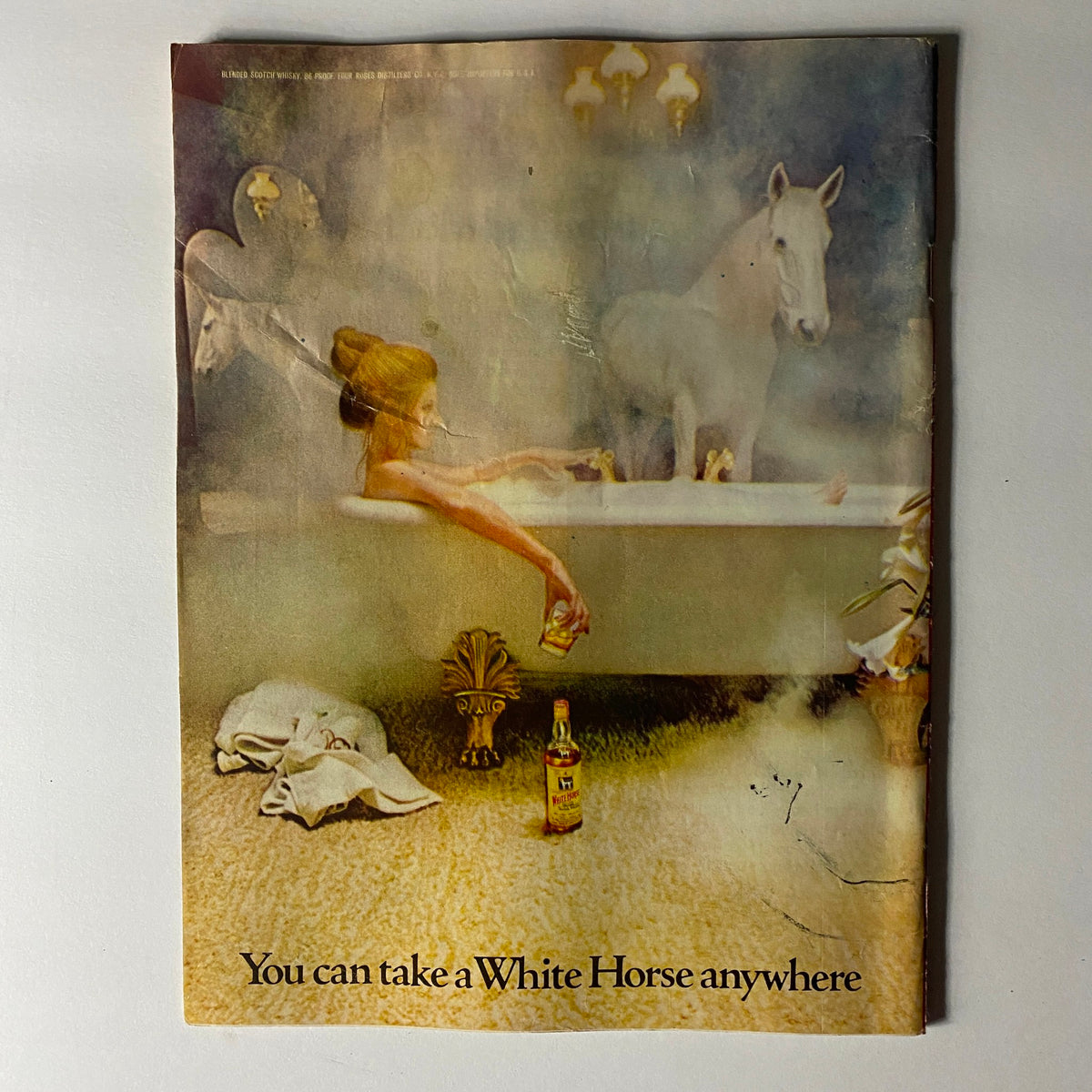 Vintage advertisement depicting a serene scene of a woman in a bathtub with a horse, promoting the concept 'You can take a White Horse anywhere'.