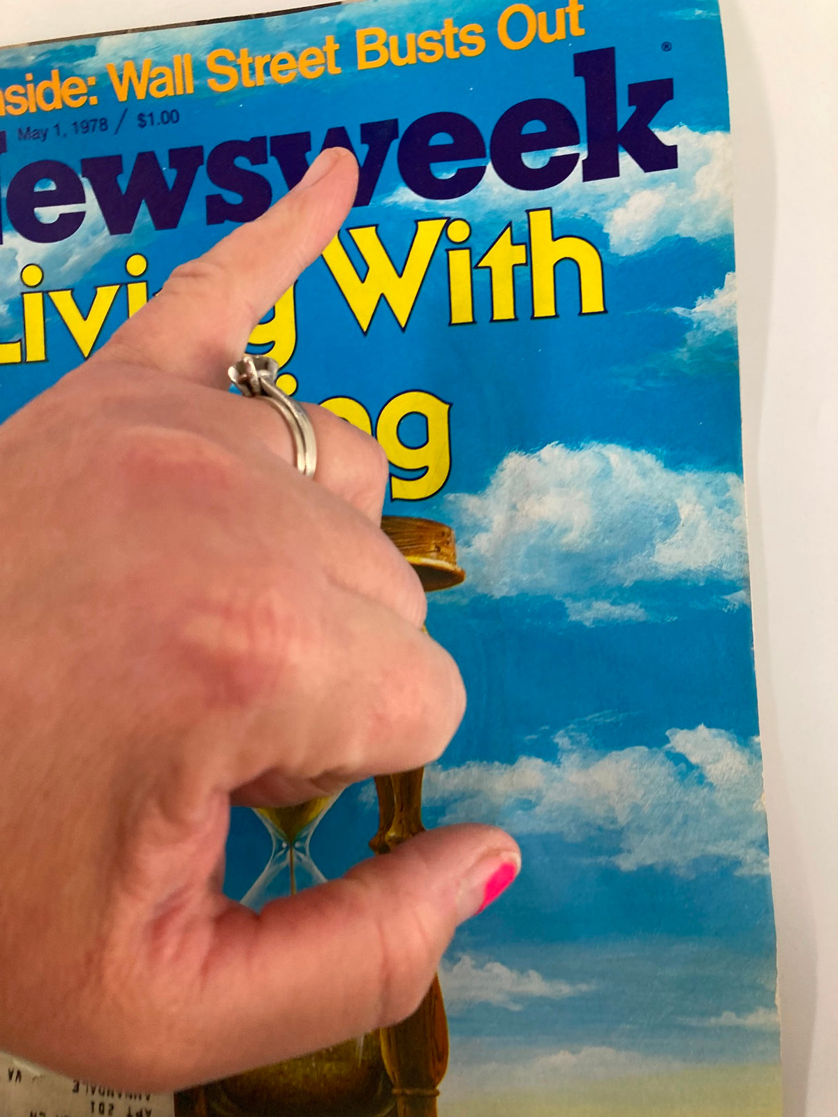 Close-up view of the vintage Newsweek magazine cover 'Living with Dying' from May 1, 1978, highlighting the hourglass and the magazine title, with a hand pointing to the title.