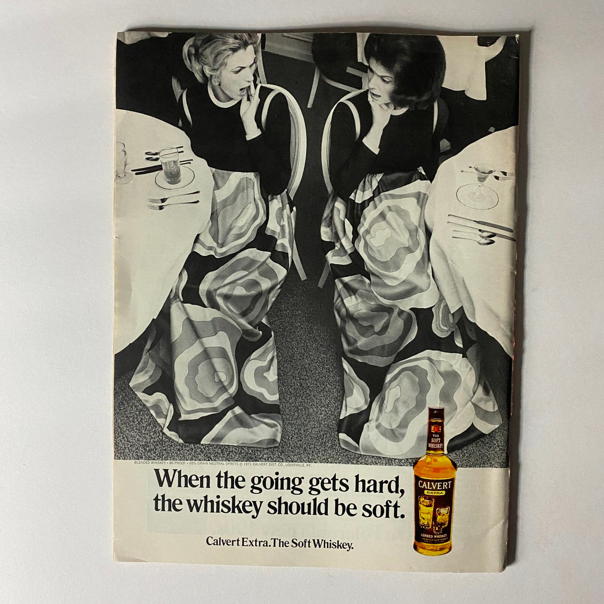 Vintage advertisement featuring two women at a dining table, promoting Calvert Extra whiskey with the slogan 'When the going gets hard, the whiskey should be soft.'