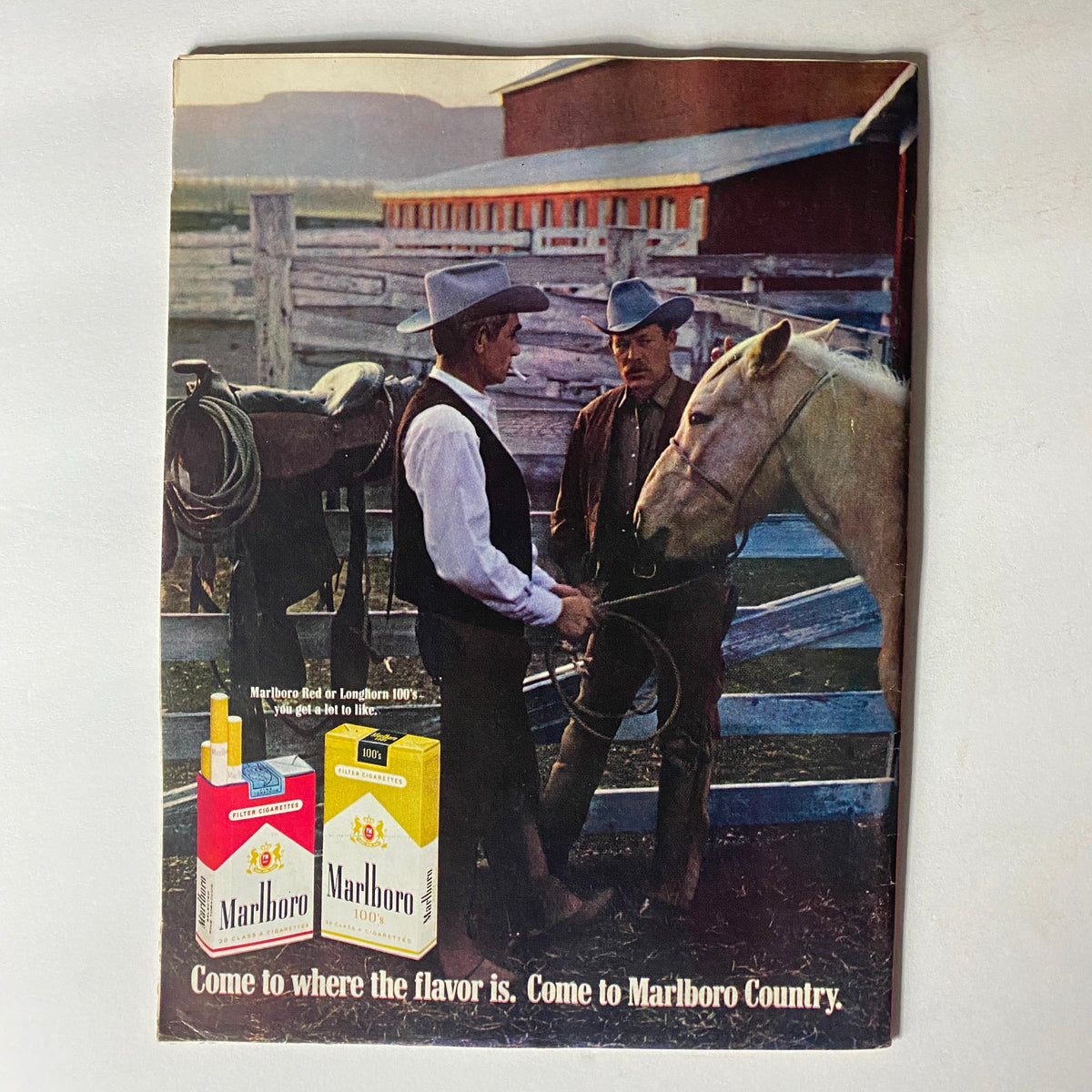 Vintage advertisement featuring Marlboro cigarettes, capturing a moment with two men in hats conversing near a horse at a ranch, promoting the slogan 'Come to where the flavor is. Come to Marlboro Country,' alongside the Vintage Time Magazine July 4 1969 cover story on César Chávez and The Grapes of Wrath.