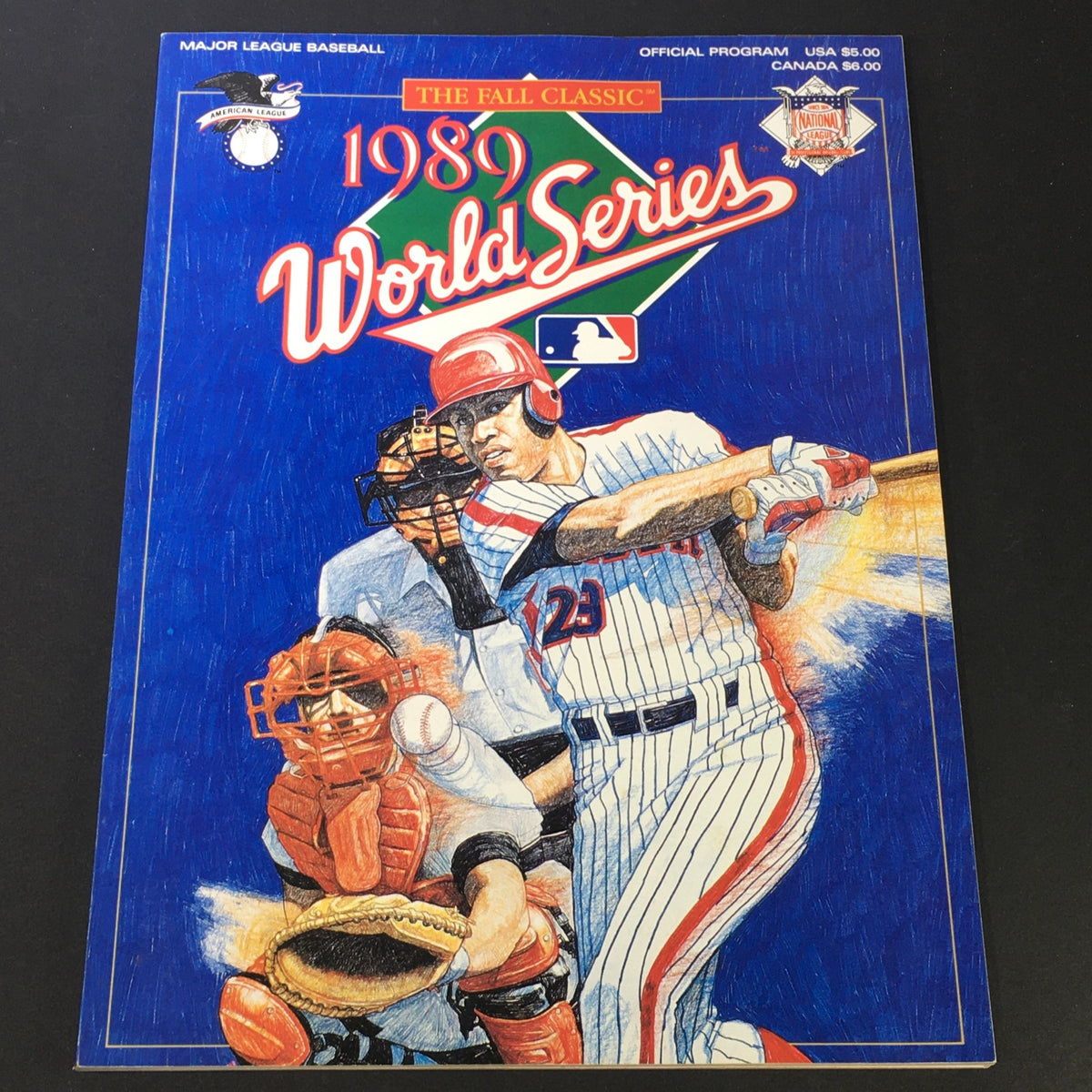 1989 Fall Classic World Series Official Program cover featuring a baseball player swinging a bat, with an illustration of a catcher in the foreground and vibrant blue background.