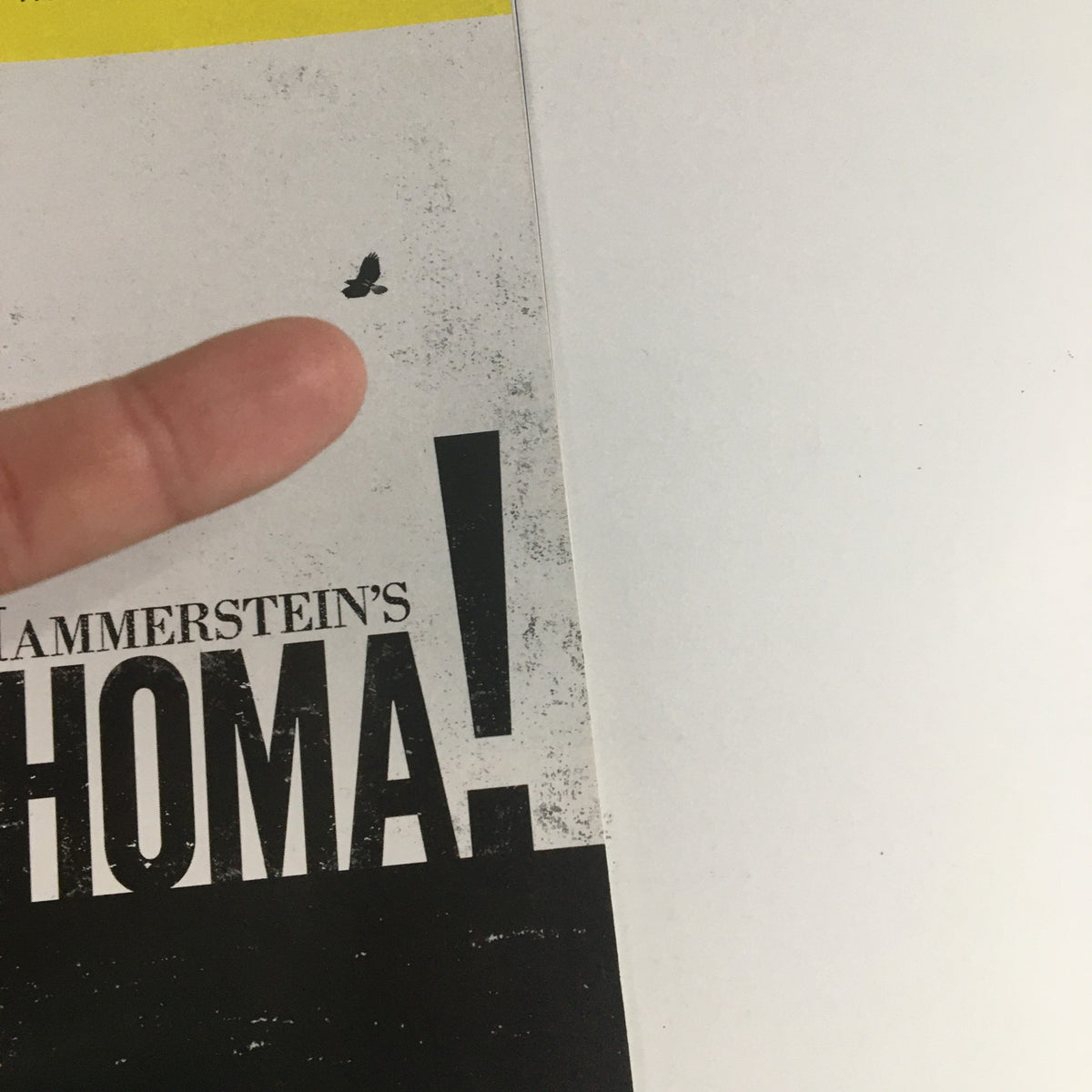 Close-up view of the 2019 Playbill Circle In The Square Present Rodgers & Hammerstein's Oklahoma, highlighting a small mark on the cover with a finger pointing to it.