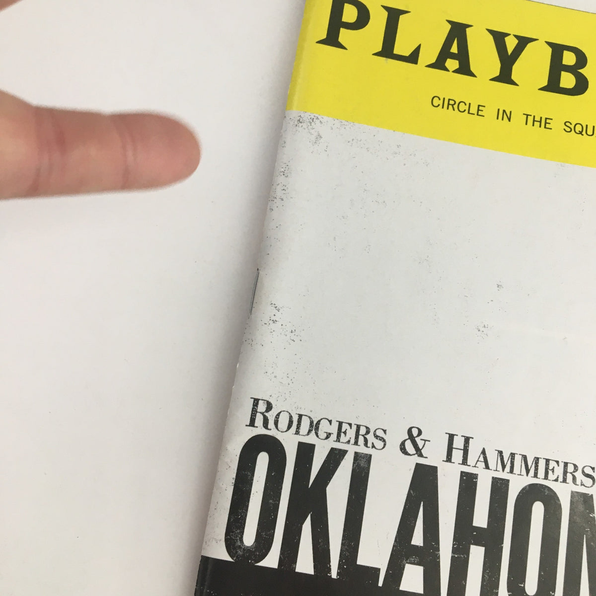 Detail image of the 2019 Playbill Circle In The Square Present Rodgers & Hammerstein's Oklahoma, showing the cover with a finger indicating the title.