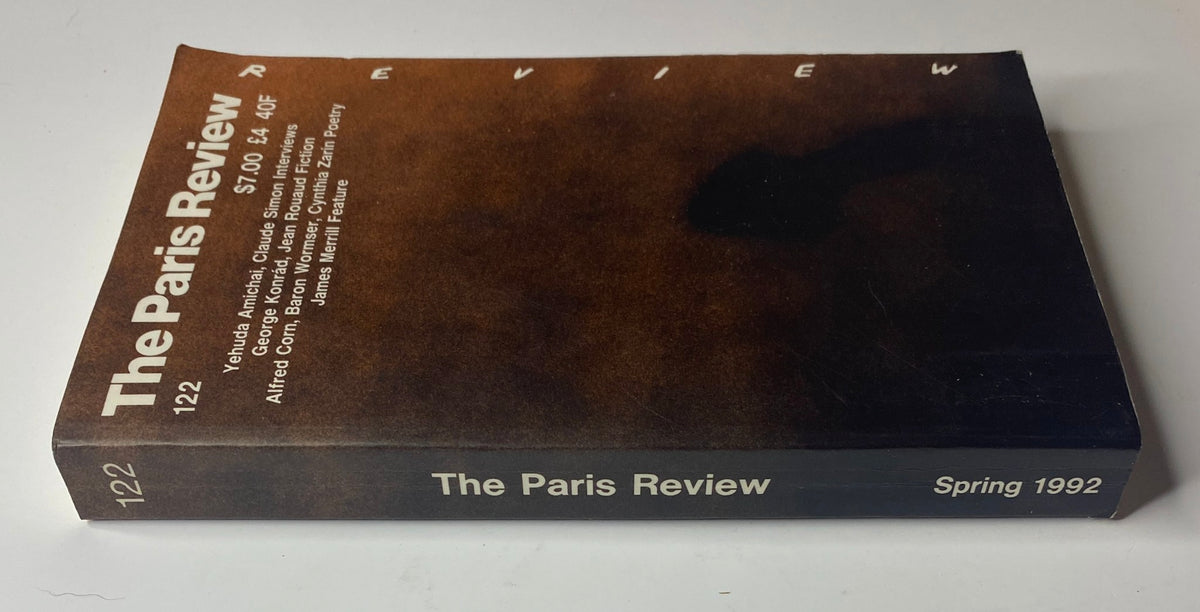 Side view of The Paris Review Magazine, Spring 1992, No. 122 showcasing its spine design. Highlighted features include contributions from George Konrád, James Merrill, and others, against a rich brown backdrop.