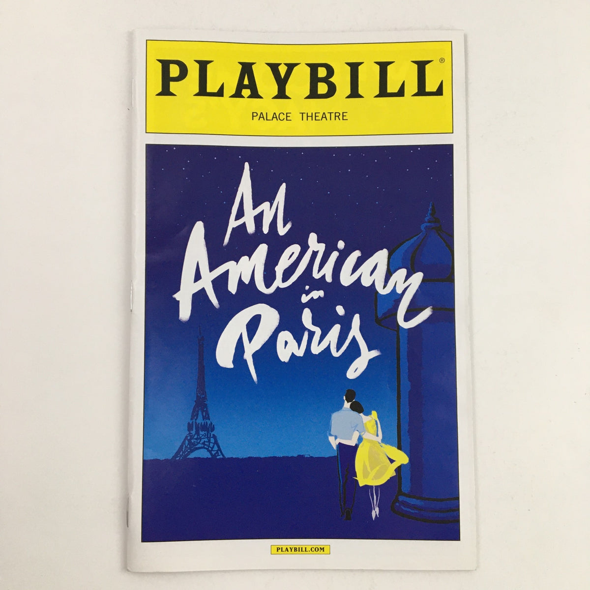 2015 Playbill for the musical An American in Paris at the Palace Theatre, featuring a romantic illustration of a couple against a backdrop of the Eiffel Tower in a night setting.