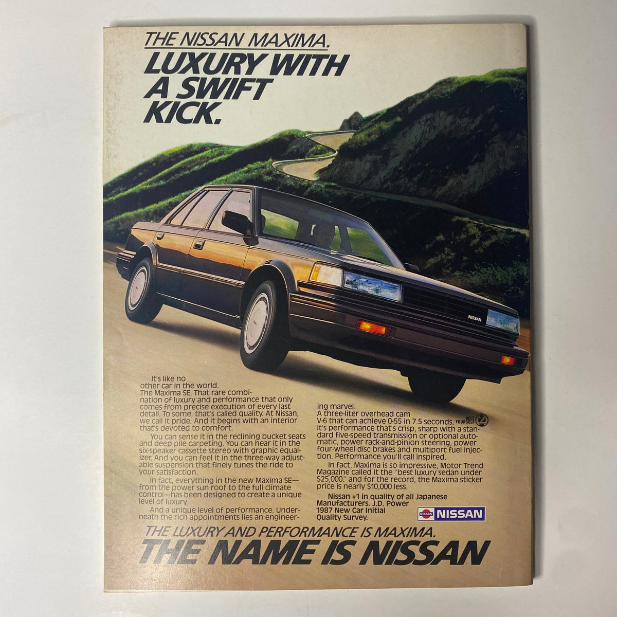 Advertisement for the Nissan Maxima in Forbes Magazine July 27, 1987, labeled 'Luxury with a Swift Kick,' featuring the vehicle on a scenic road, promoting its performance and luxury features.