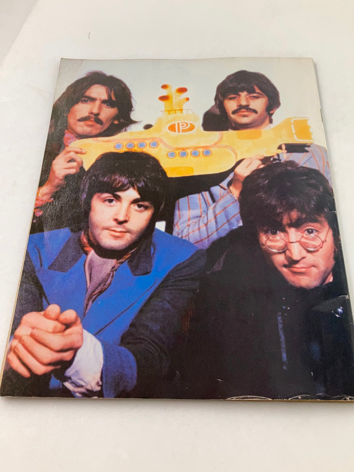 Image from the 1981 John Lennon Beatles Memory Book depicting The Beatles posing with a yellow submarine prop, showcasing the band's iconic style and legacy.