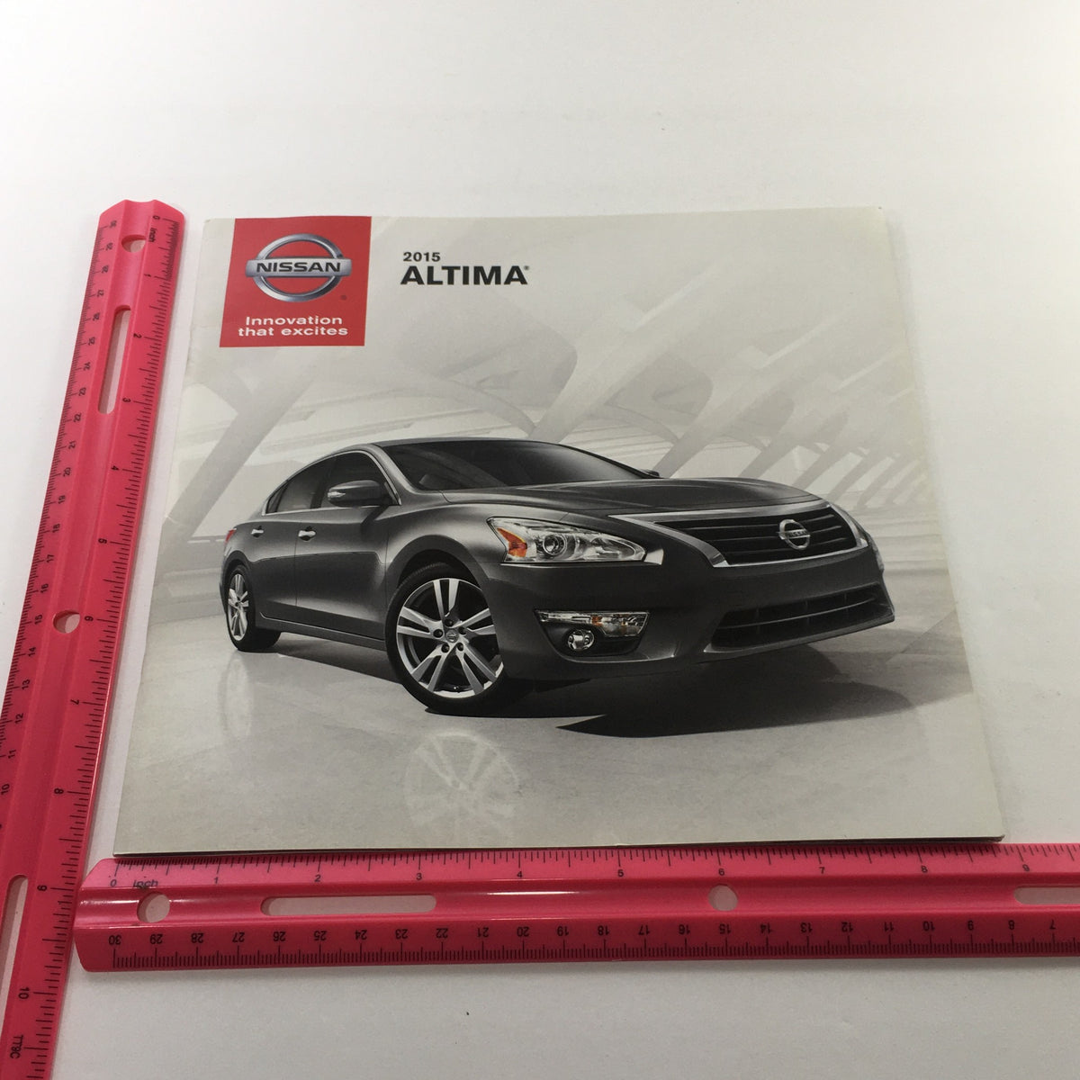 Front cover of the 2015 Nissan Altima Sedan Dealership Car Auto Brochure Catalog, highlighting a sleek black Nissan Altima parked in a modern setting.