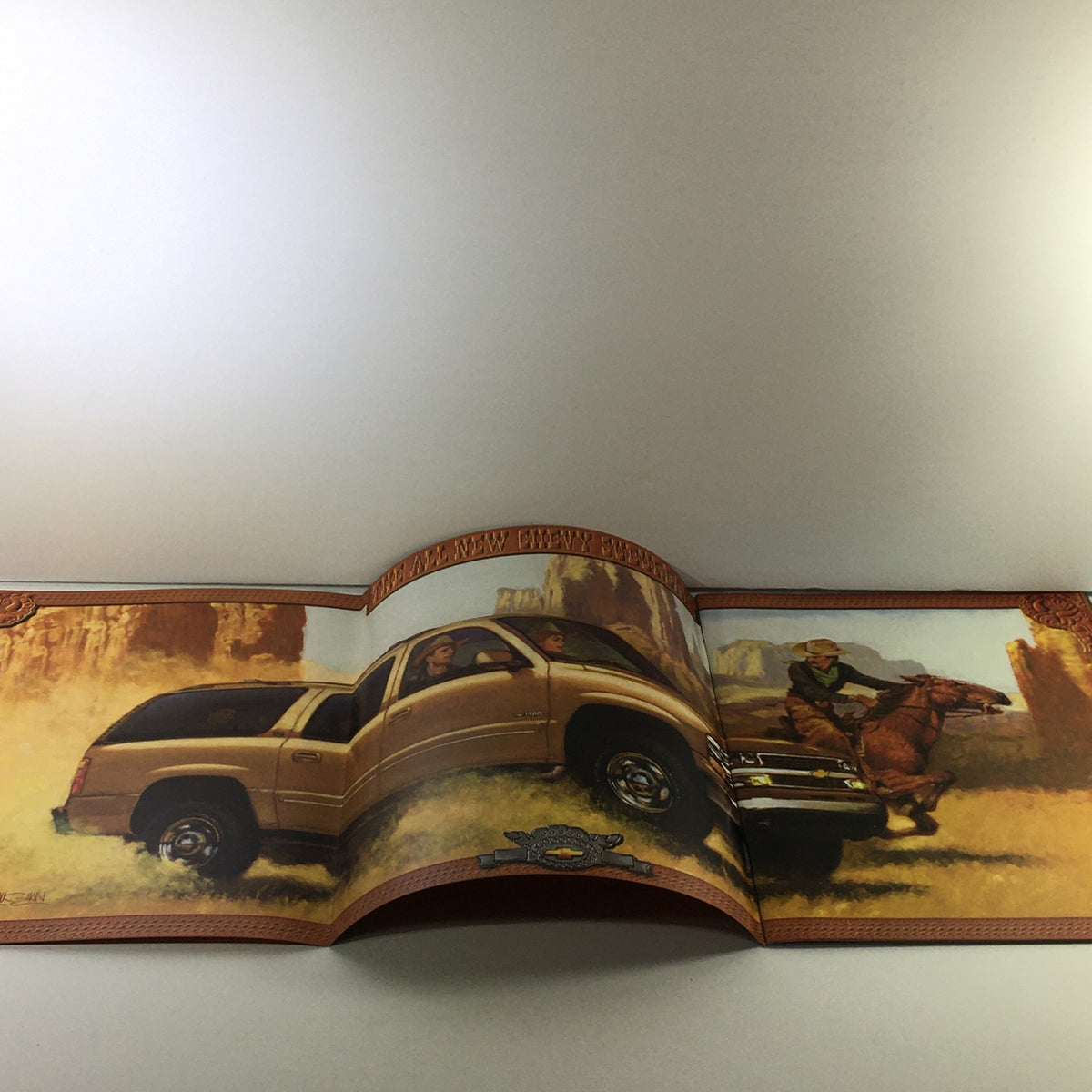 2000s Chevrolet Chevy Suburban Dealership Car Auto Brochure Catalog featuring an open brochure with a golden Chevrolet Suburban showcased in a scenic landscape.