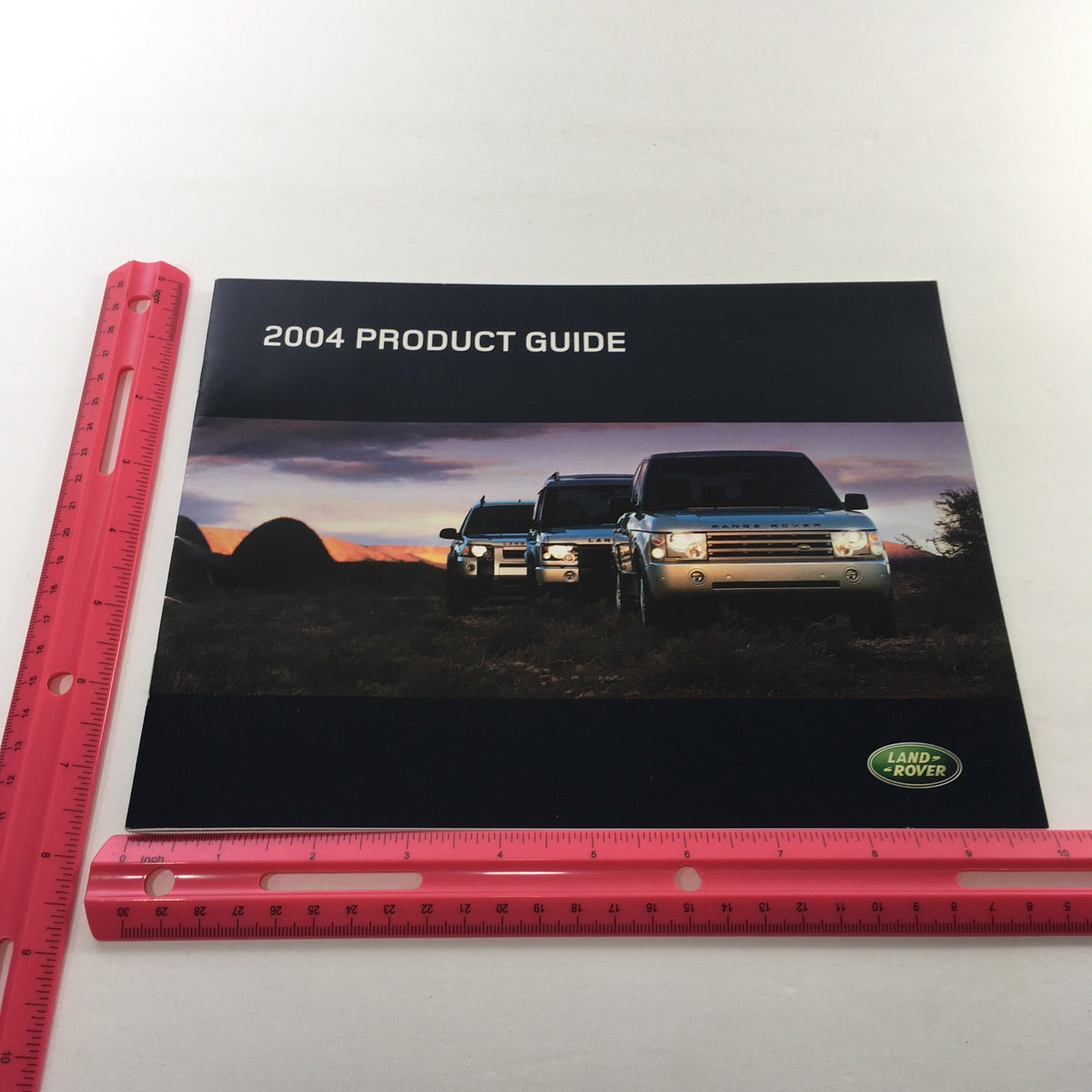 Front view of the 2004 Land Rover Product Guide displaying two Land Rover vehicles, with a ruler for size reference, emphasizing its importance in this dealership car auto brochure catalog.
