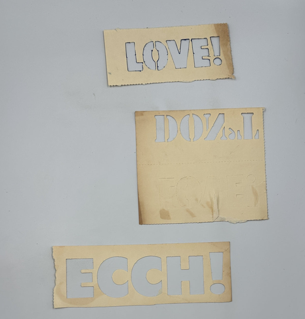 Stencils from MAD Magazine's 1967 Follies 5 Fifth Annual Collection featuring the words 'LOVE!', 'DOZ.L', and 'ECCH!'. These artistic cut-outs are part of the collectible stencils included in the magazine.