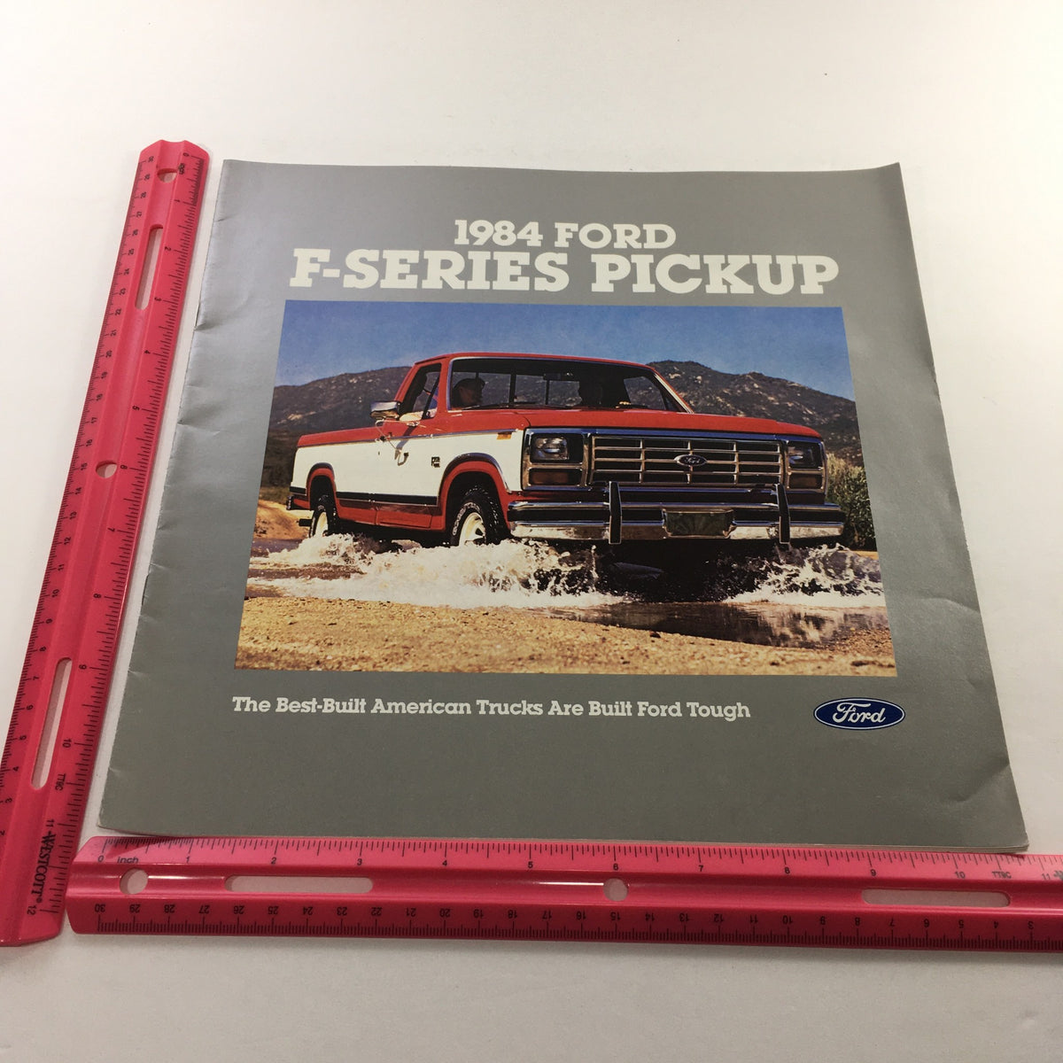 1984 Ford F-Series Pickup Dealership Car Auto Brochure Catalog displaying a red Ford pickup truck splashing through water with mountains in the background, emphasizing the durability of Ford trucks.