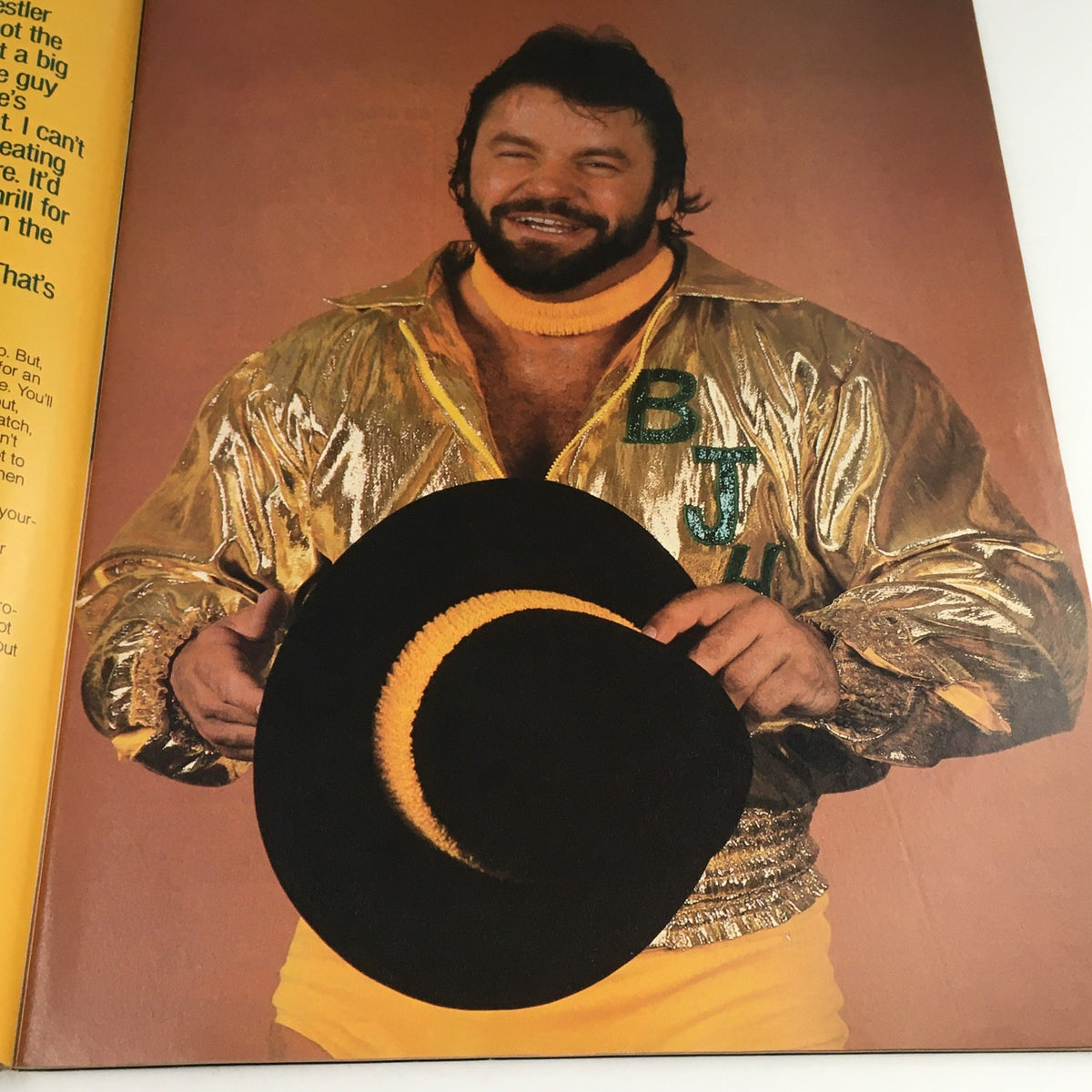 WWF Magazine December 1986 image of a smiling wrestler in a shiny gold jacket, holding a black hat, capturing the charismatic personalities of wrestling legends from the era.