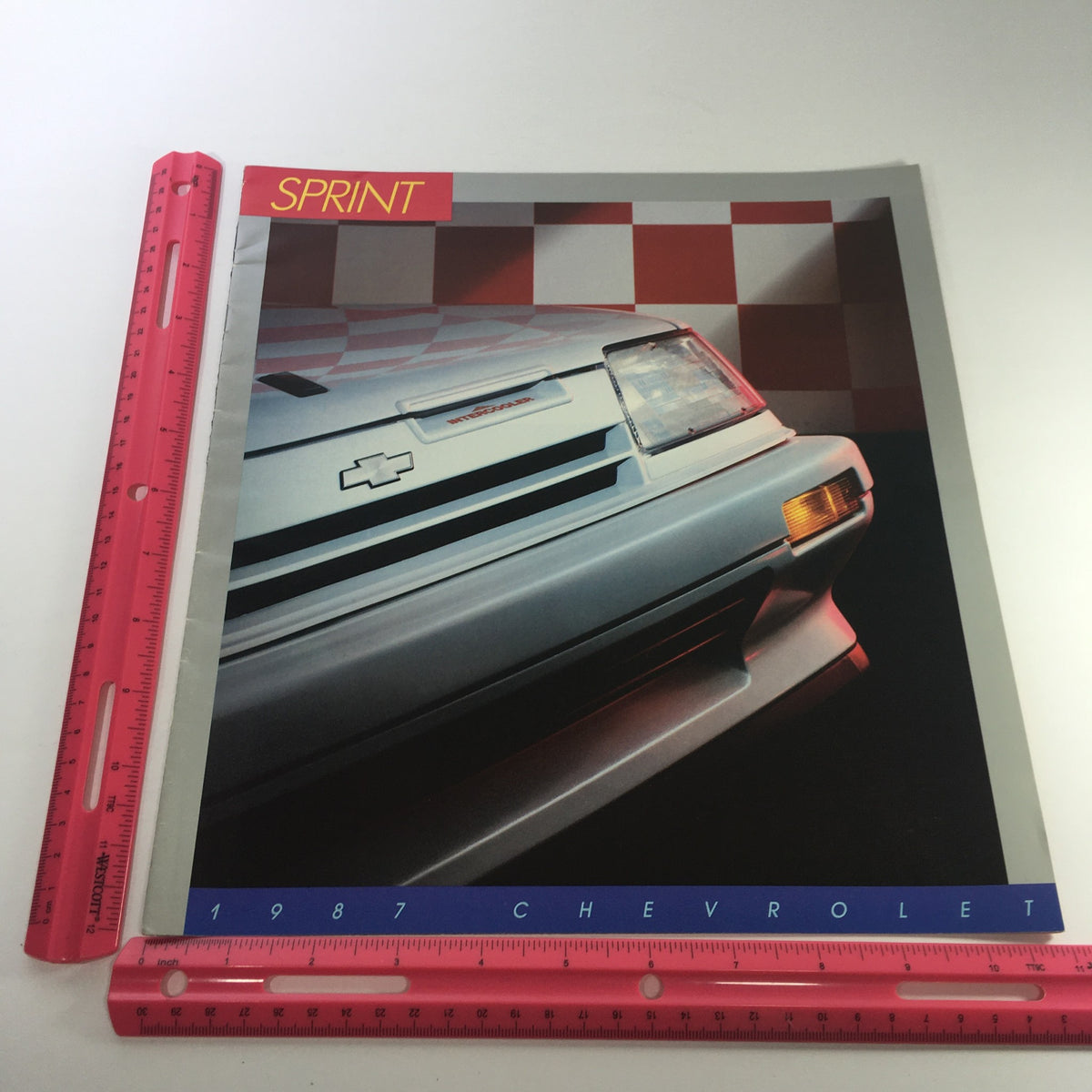 1987 Chevrolet Sprint brochure featuring a dynamic view of the car with a ruler for size reference, part of a lot of 8 dealership car brochure catalogs.