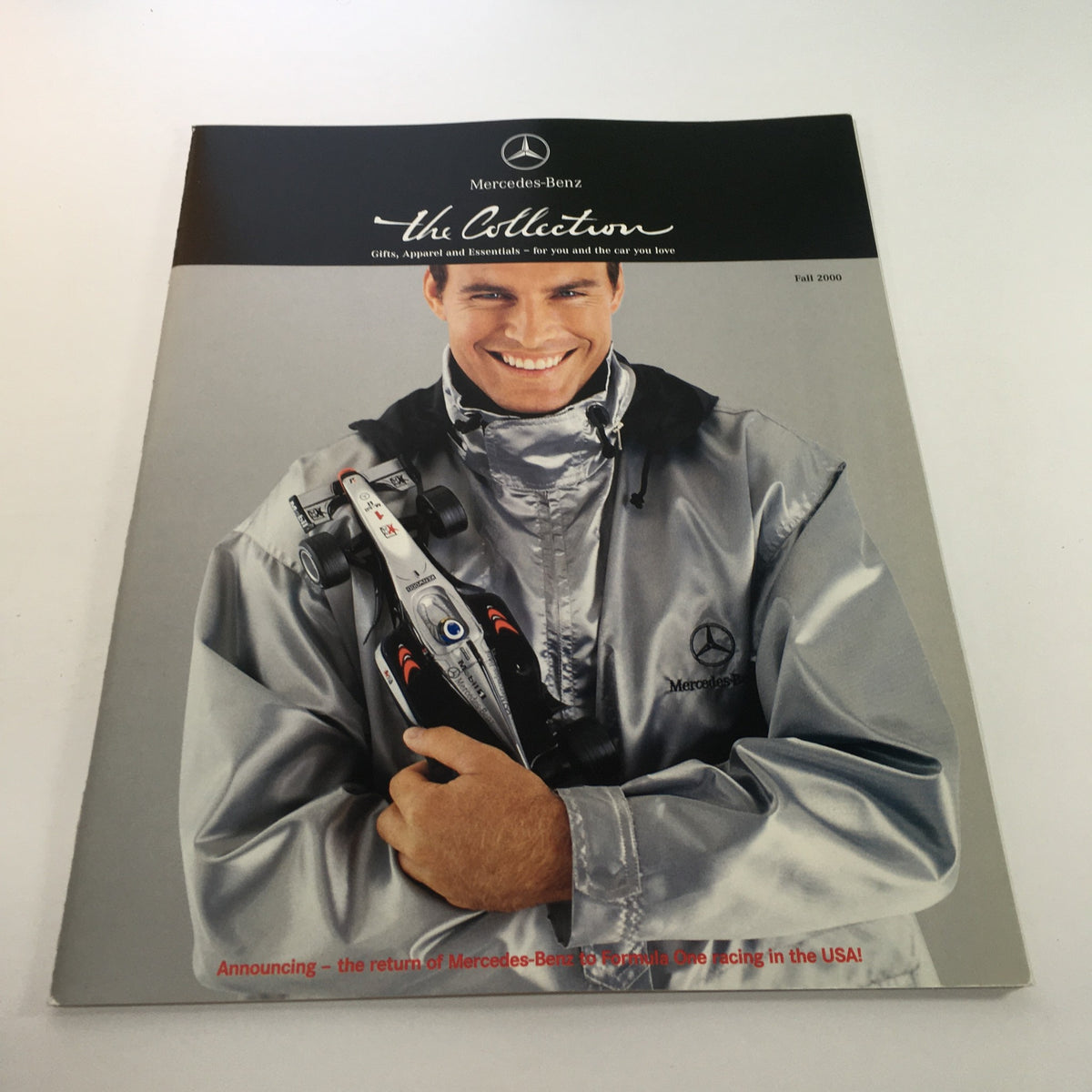 Image from the 2000 Mercedes-Benz Welcome Lease and Finance The Collection Dealership Catalog featuring a smiling model in a grey jacket with a toy car, highlighting the return of Mercedes-Benz racing in the USA.