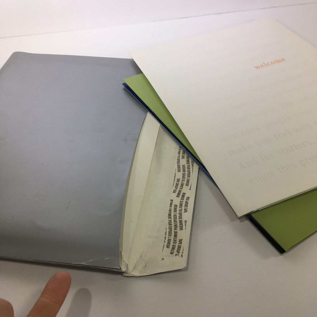 Inside view of the 2000 Mercedes-Benz Welcome Lease and Finance The Collection Dealership Catalog with visible wear on the cover and pages, including a silver folder holding various documents.