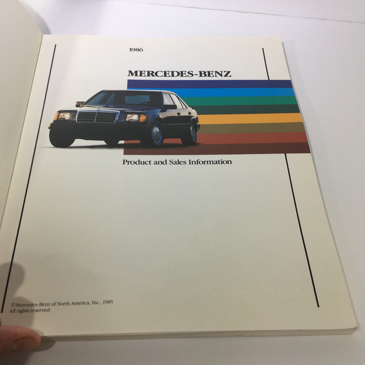 1986 Mercedes-Benz Product and Sales Information Brochure cover featuring a classic Mercedes-Benz vehicle with a colorful striped background.
