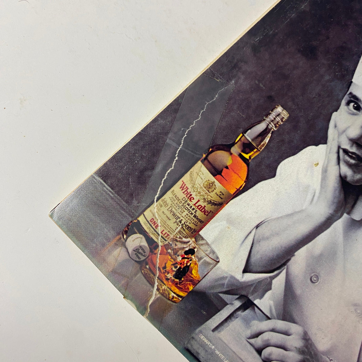 Close-up image from Forbes Magazine January 28, 1985 of Dewar's Profile featuring a whiskey bottle next to chef Jean-Claude Nédélec, showcasing marketing and culinary culture of the time.
