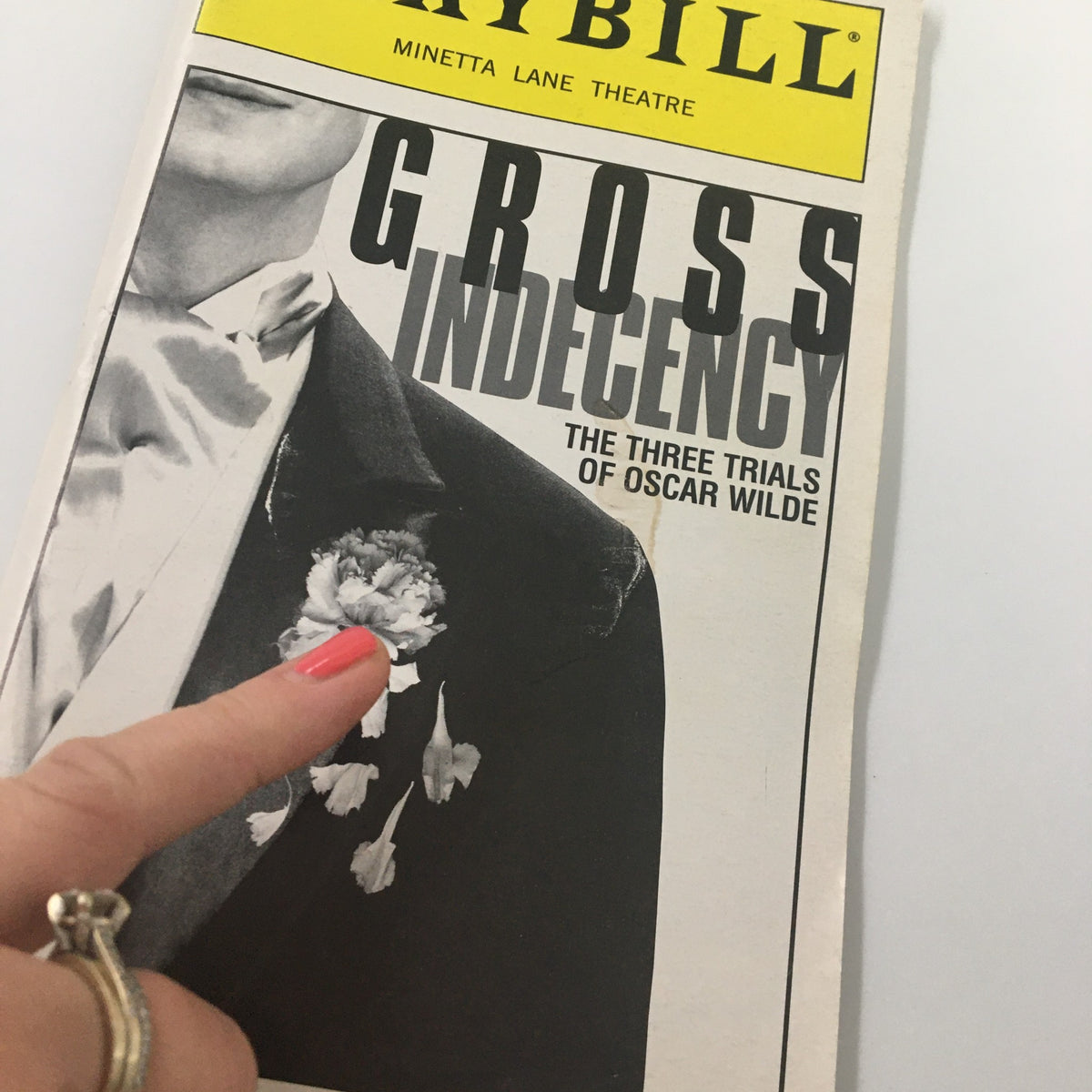 Close-up of the 1997 Playbill for Gross Indecency: The Three Trials of Oscar Wilde, highlighting the cover and a finger pointing at the flower detail.