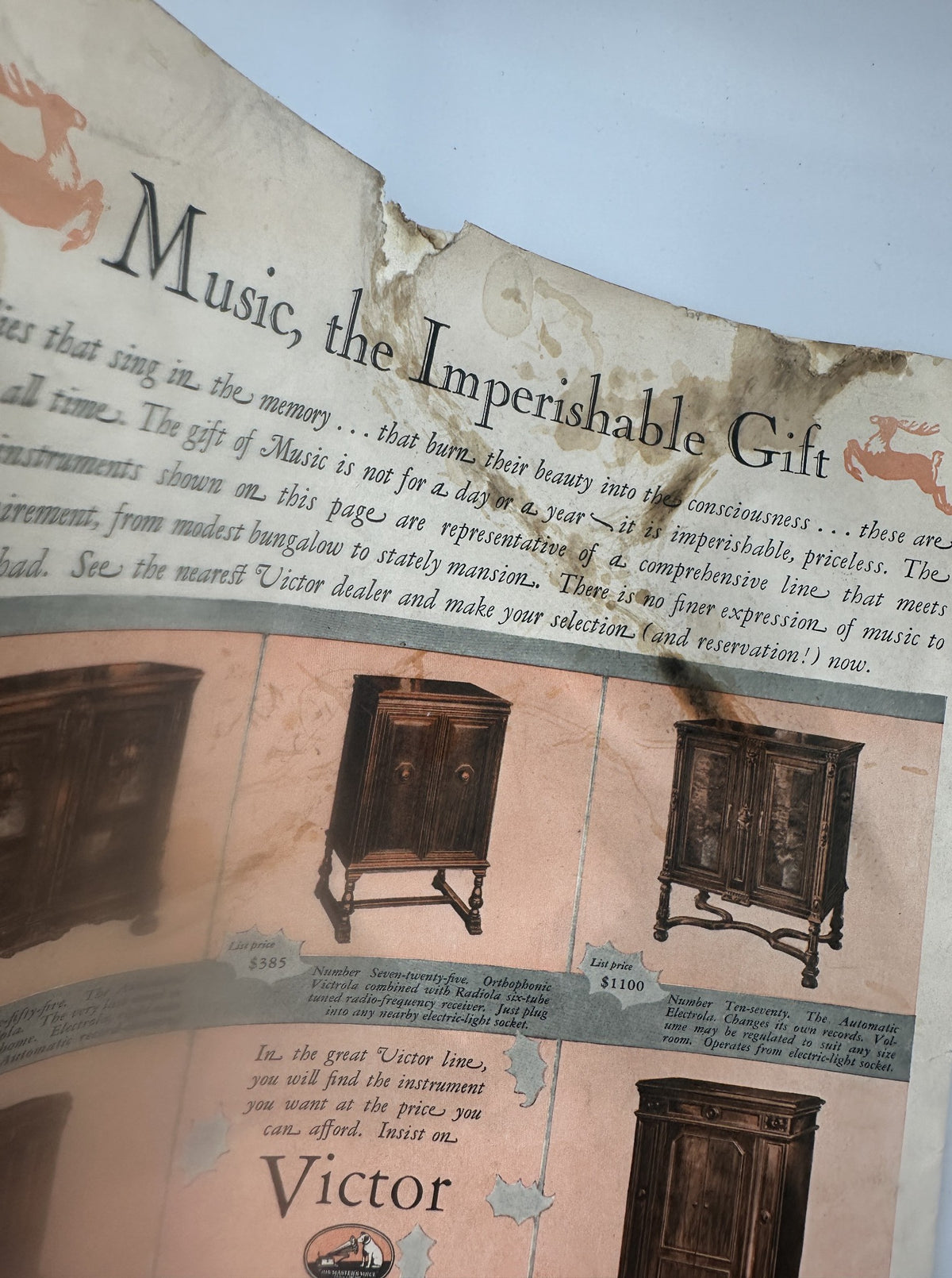 Vintage advertisement titled 'Music the Imperishable Gift' from Collier’s Magazine December 17, 1927, featuring descriptions of Victor audio furniture with noticeable wear and water stains.