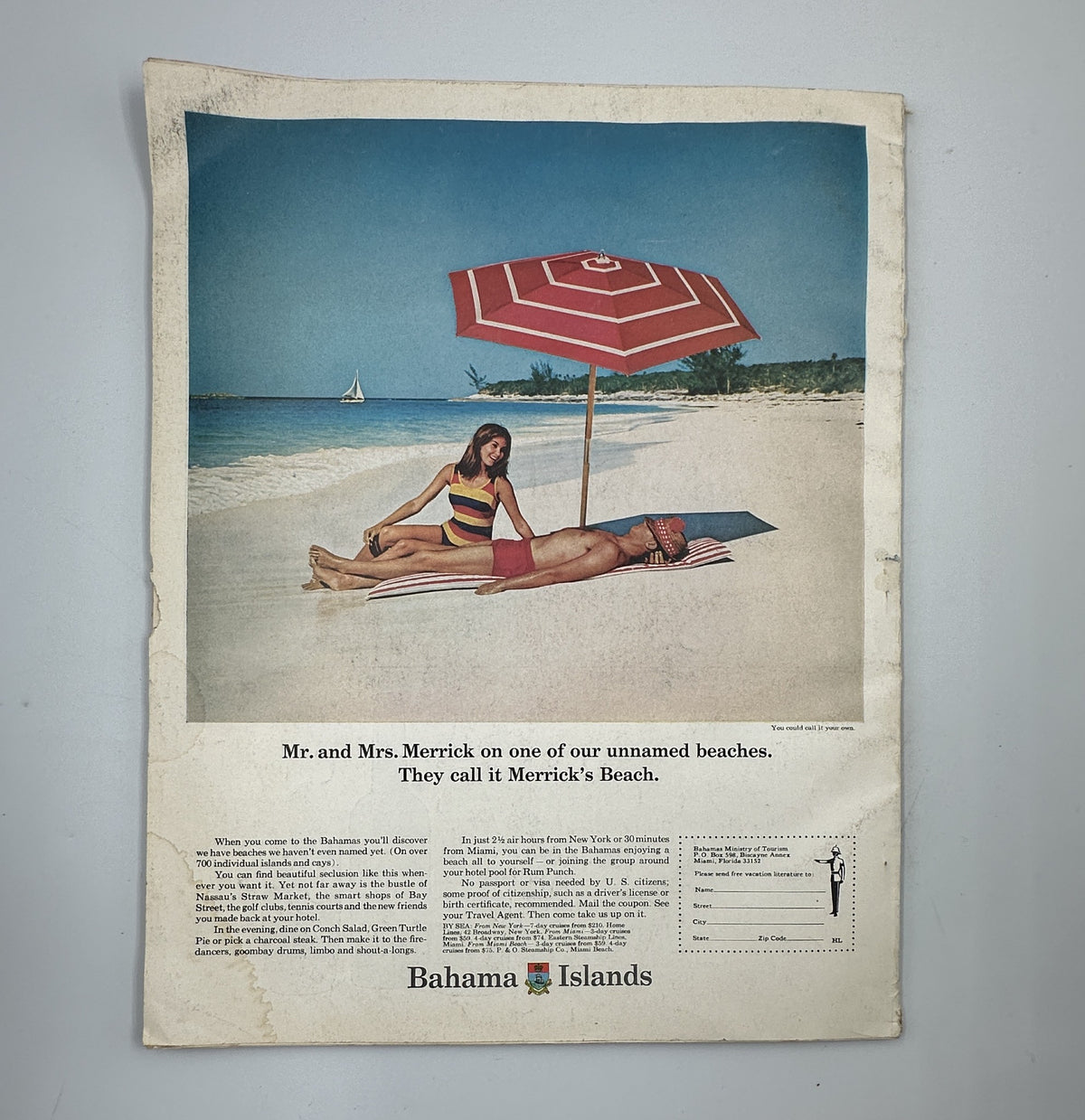 Vintage advertisement from Holiday Magazine November 1967 promoting the Bahamas, featuring a beach scene with Mr. and Mrs. Merrick enjoying the sun, accompanied by a large umbrella.