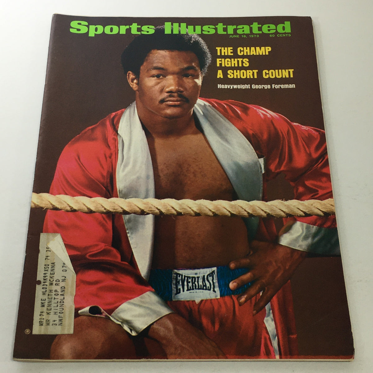 Cover of Sports Illustrated magazine from June 18, 1973, featuring heavyweight boxer George Foreman, who is seen wearing a red boxing robe and standing in a boxing ring, with the title 'The Champ Fights A Short Count' prominently displayed.