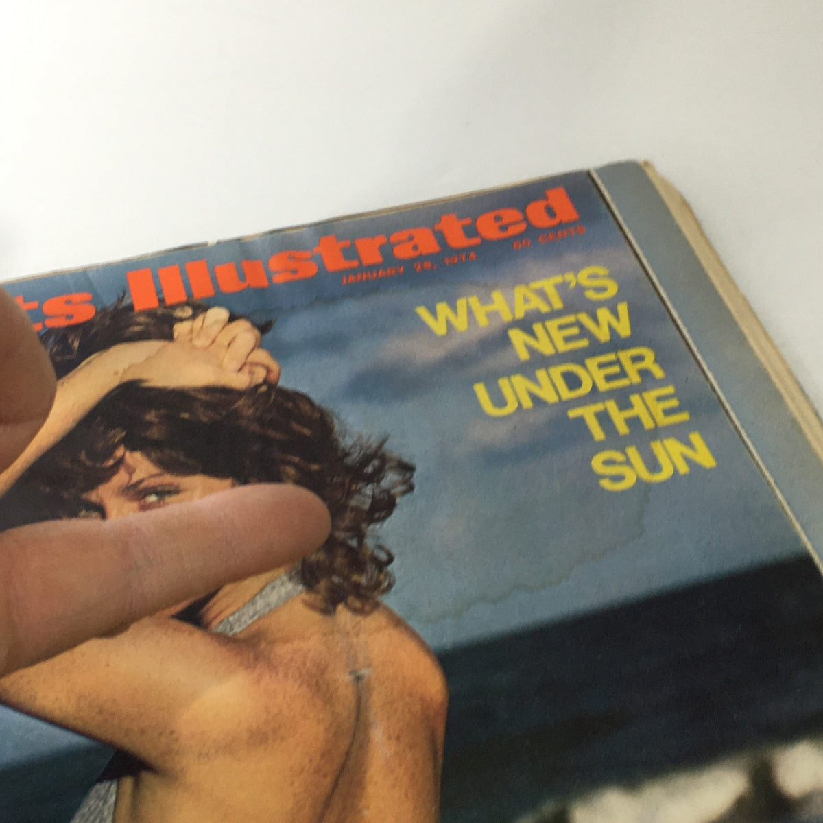 Detailed close-up of the Sports Illustrated magazine cover from January 28, 1974, highlighting the woman in a bikini and focusing on the text 'What's New Under The Sun,' with a hand partially obscuring the cover.