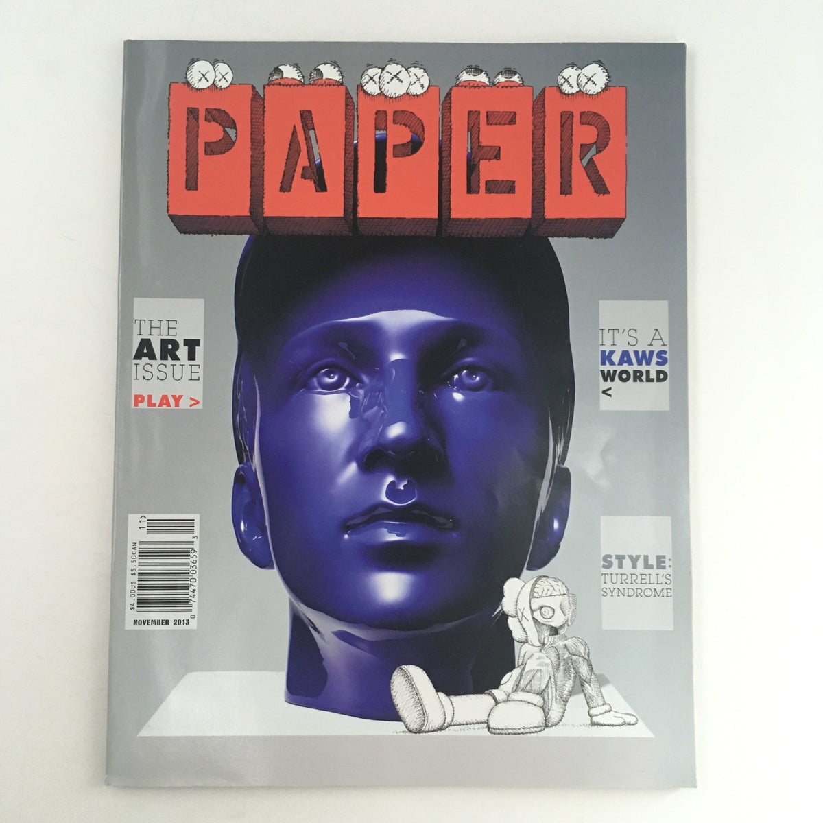 Cover of Paper Magazine November 2013: The Art Issue & It's A Kaws World featuring a stylized blue bust sculpture and graphic title, reflecting the intersection of contemporary art and pop culture.