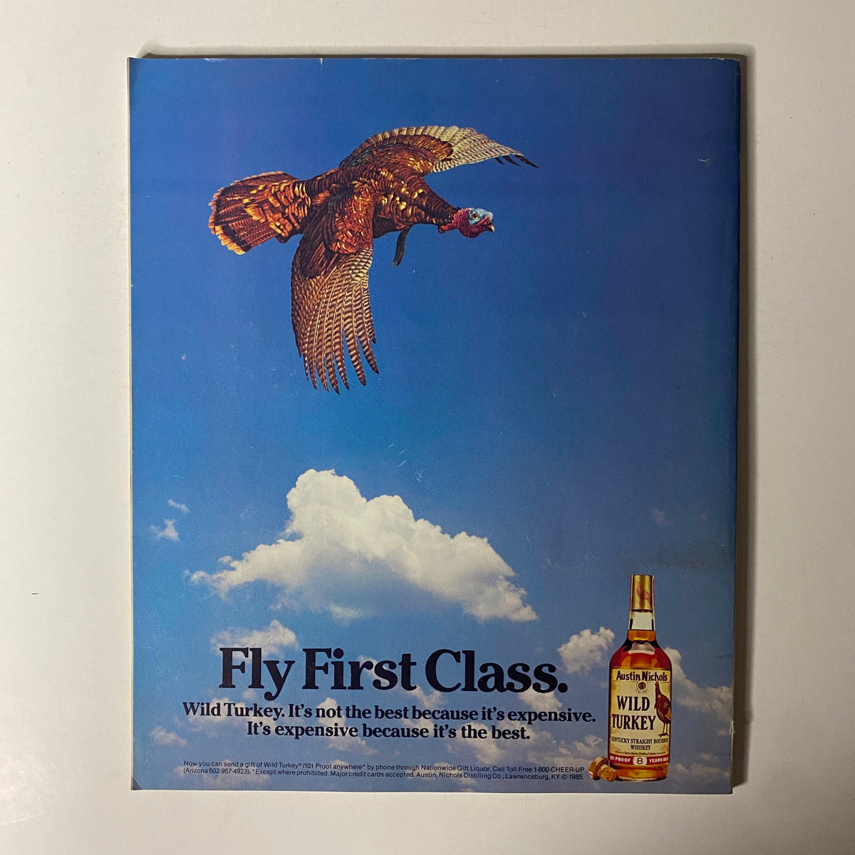 Vintage advertisement for Wild Turkey featuring a flying turkey with the slogan 'Fly First Class.' It emphasizes the quality of Wild Turkey whiskey, stating 'It's not the best because it's expensive. It's expensive because it's the best,' dated February 1985.