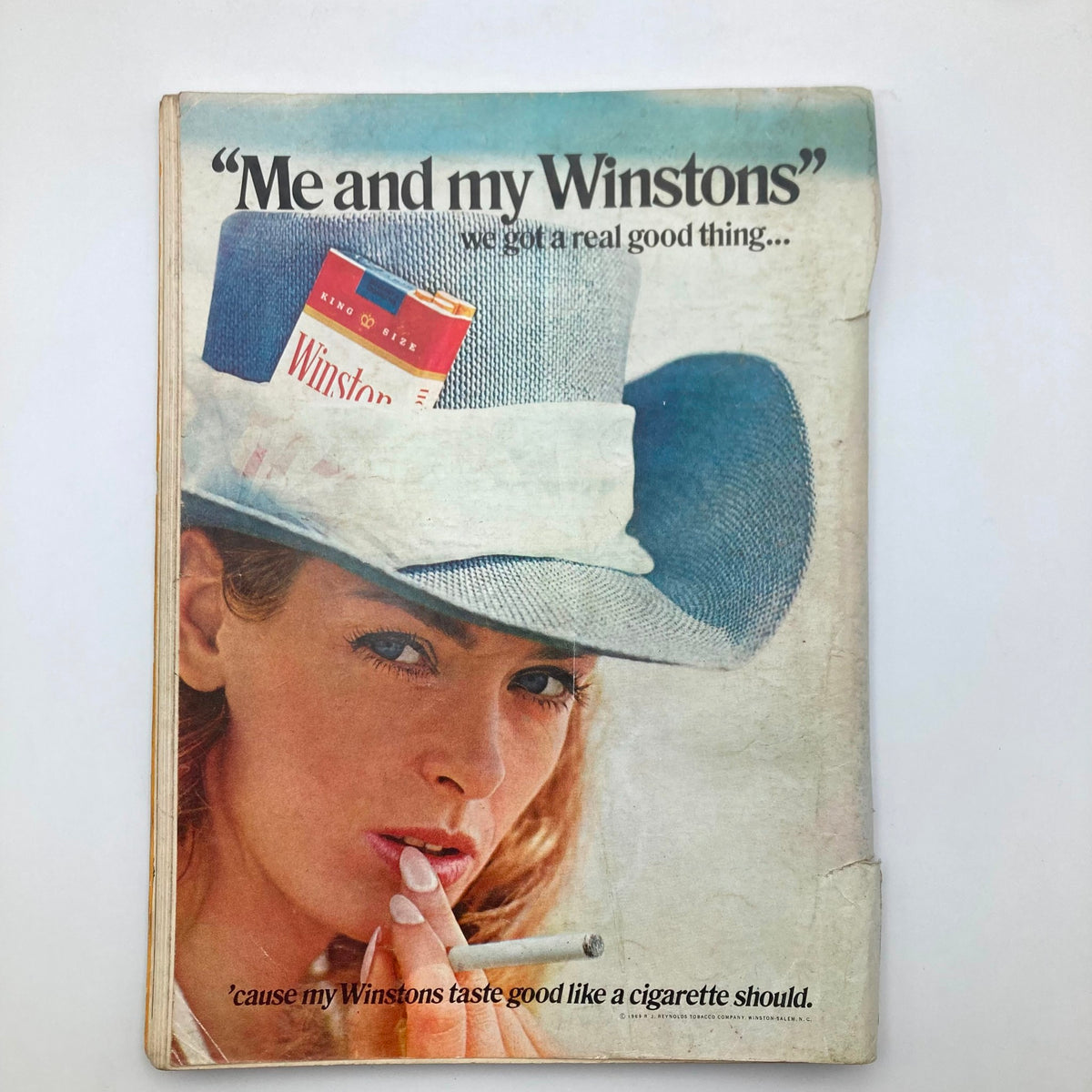 Advertisment page from the Vintage Playboy Magazine August 1969 featuring a woman in a stylish blue hat with a Winston cigarette, evoking retro advertising aesthetics.