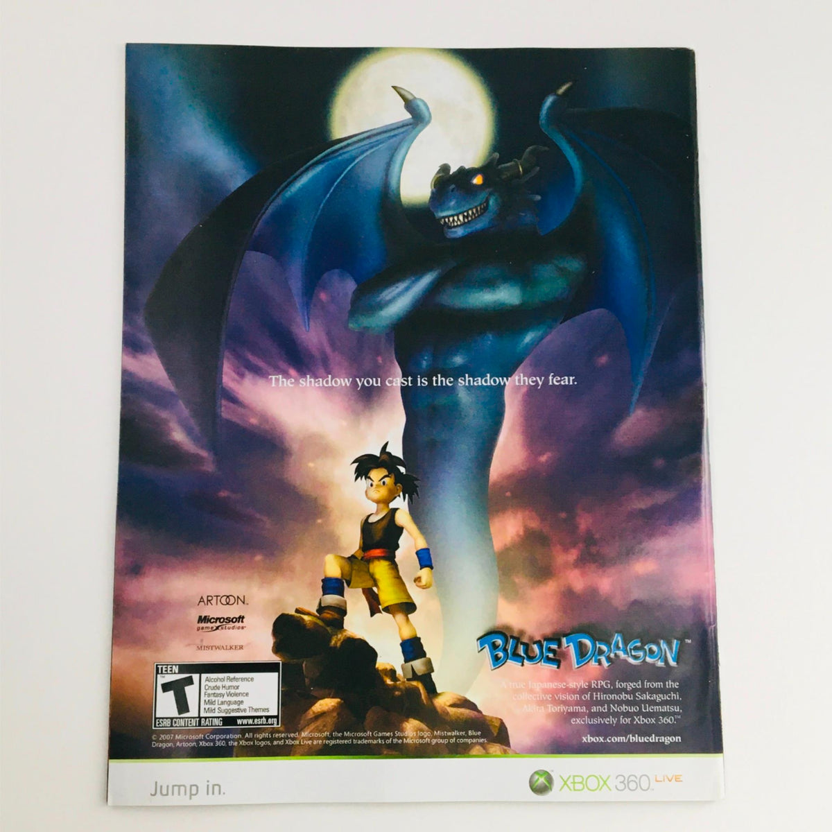 Promotional advertisement for Blue Dragon video game featuring a character standing confidently under a menacing dragon shadow, highlighting the RPG genre and the game's intriguing atmosphere.