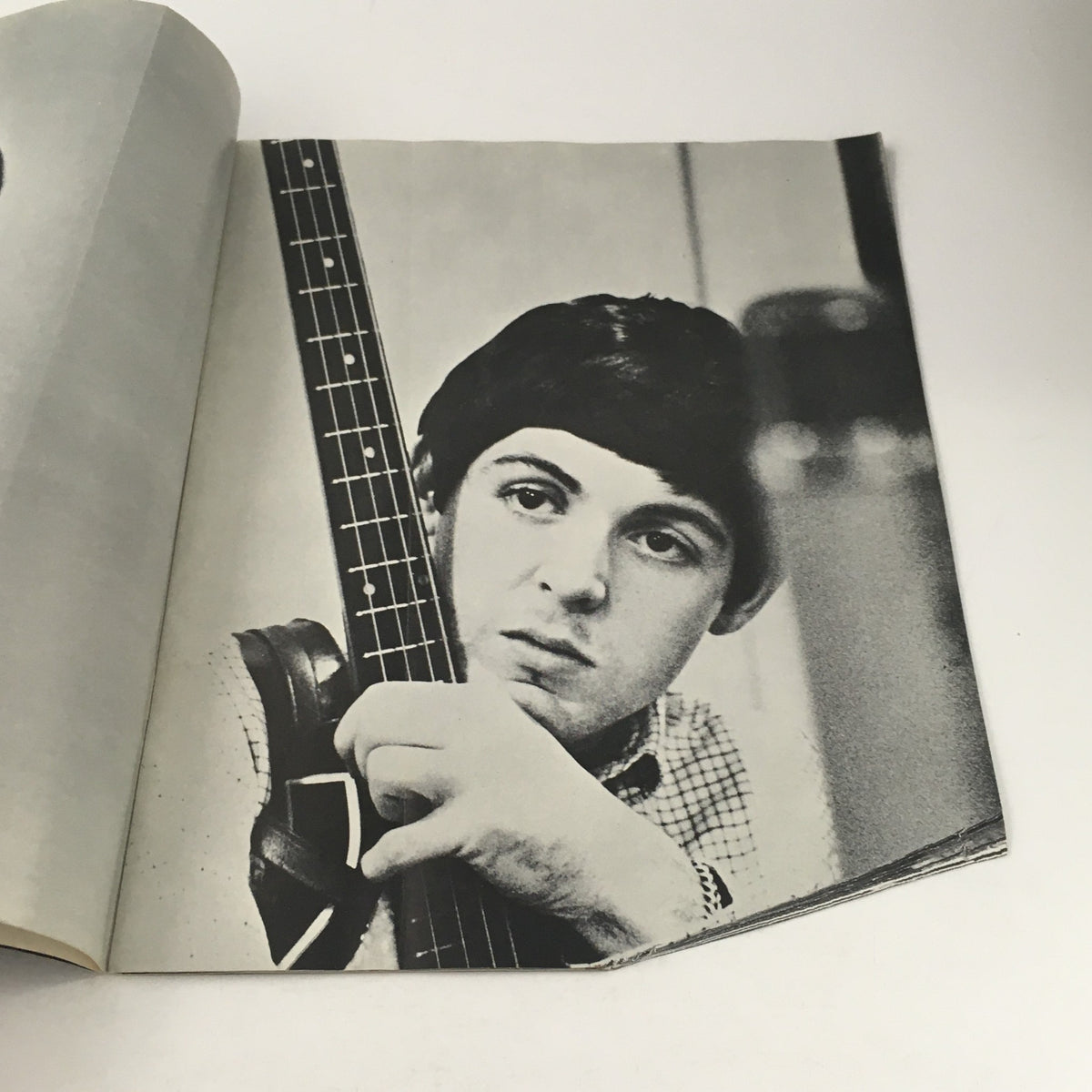 Black and white image of a young Paul McCartney holding a bass guitar, showcasing his expression, from 1964 magazine featuring The Beatles by Norman Parkinson.