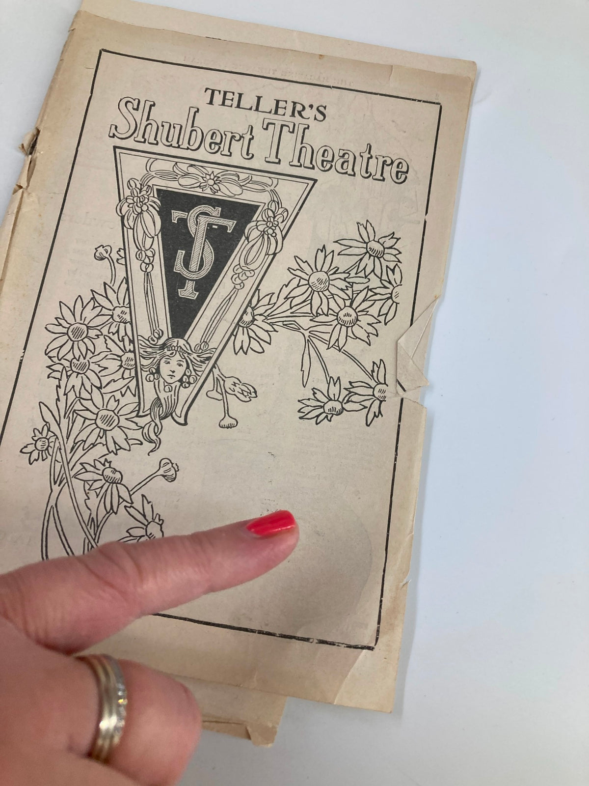 Close-up of the front cover of the 1921 Teller's Shubert Theatre playbill for 'Spanish Love' with a hand pointing at the design.