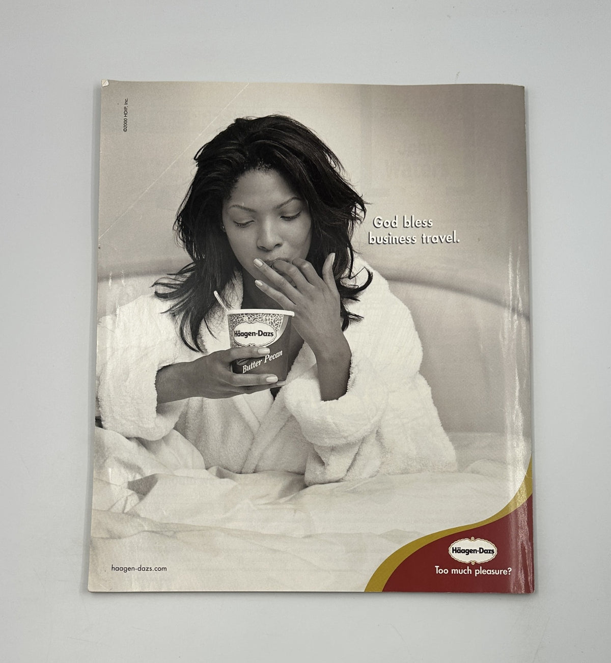 Advertisement for Haagen-Dazs ice cream featuring a woman in a bathrobe enjoying ice cream in bed with the caption 'God bless business travel.' This ad reflects a luxurious and indulgent lifestyle.