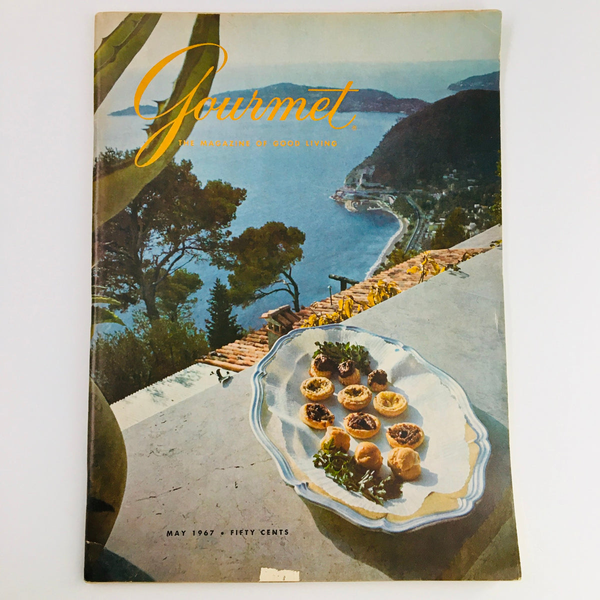 Gourmet Magazine of Good Living May 1967 cover featuring a scenic view with a coastal landscape and elegant hors d'oeuvres on a plate.